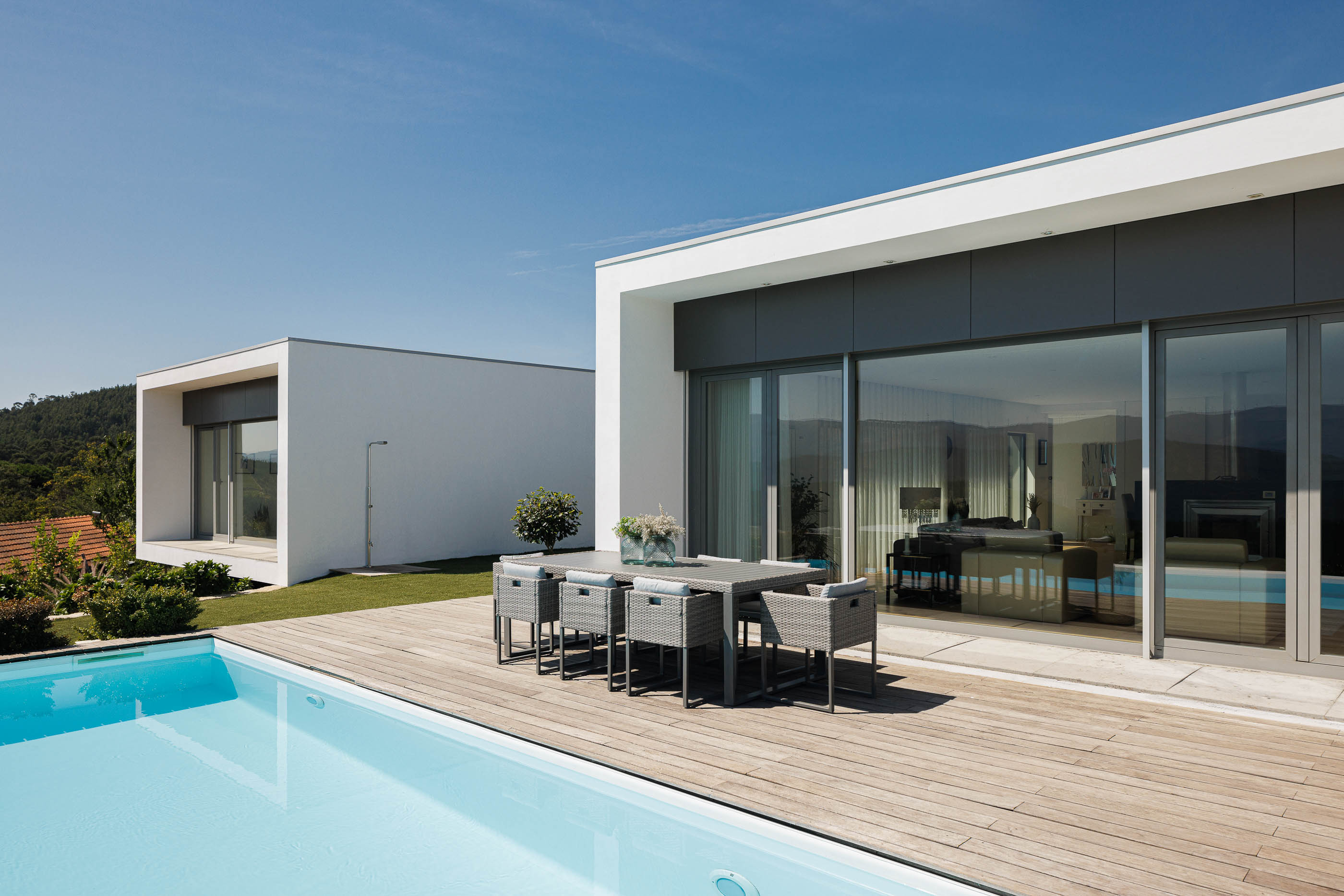 Exterior: Piscina com deck de madeira, mesa de refeições e vista panorâmica. Fachada branca da casa com grandes janelas. — Casa do Alto arquitetura Jorge Martins arquiteto em Celorico de Basto