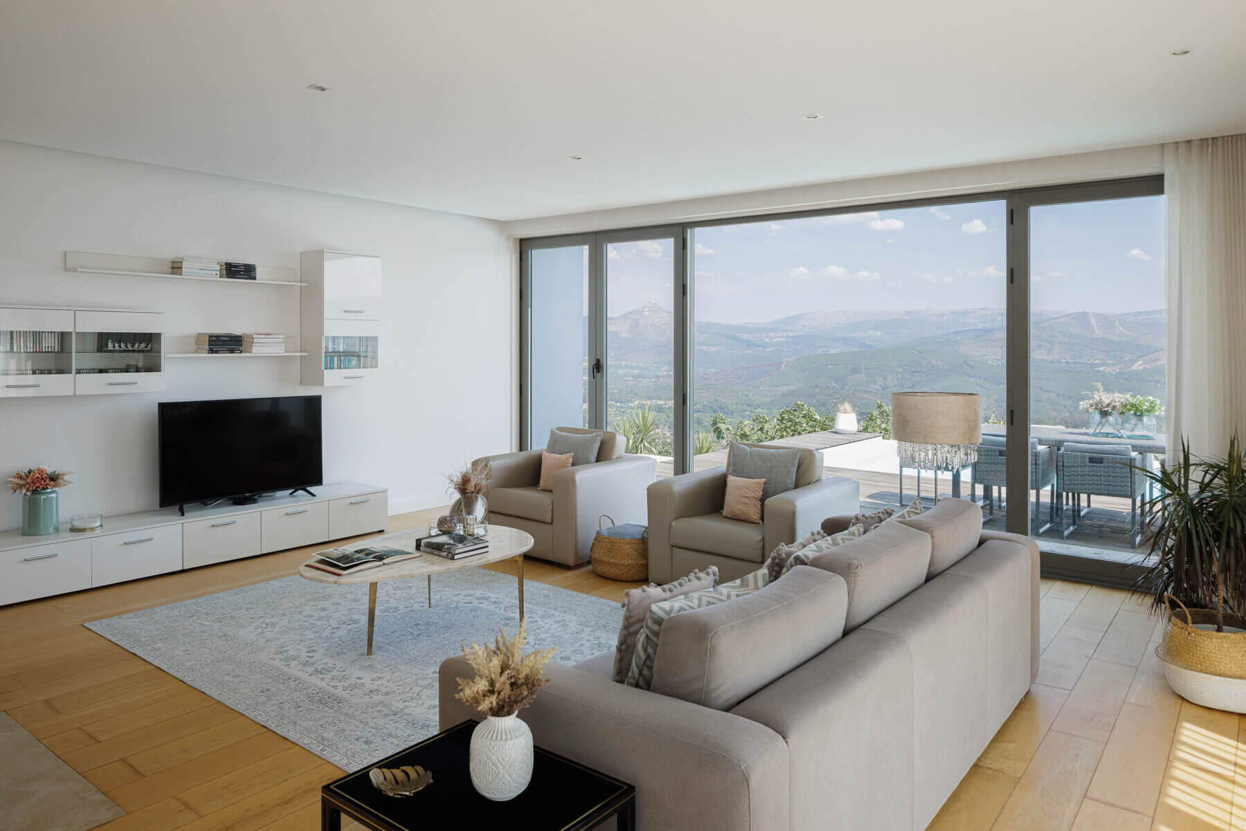 Sala de estar: Sofá e cadeirões em tons neutros, alcatifa clara, móveis brancos e grande janela com vista para o exterior. — Casa do Alto arquitetura Jorge Martins arquiteto em Celorico de Basto