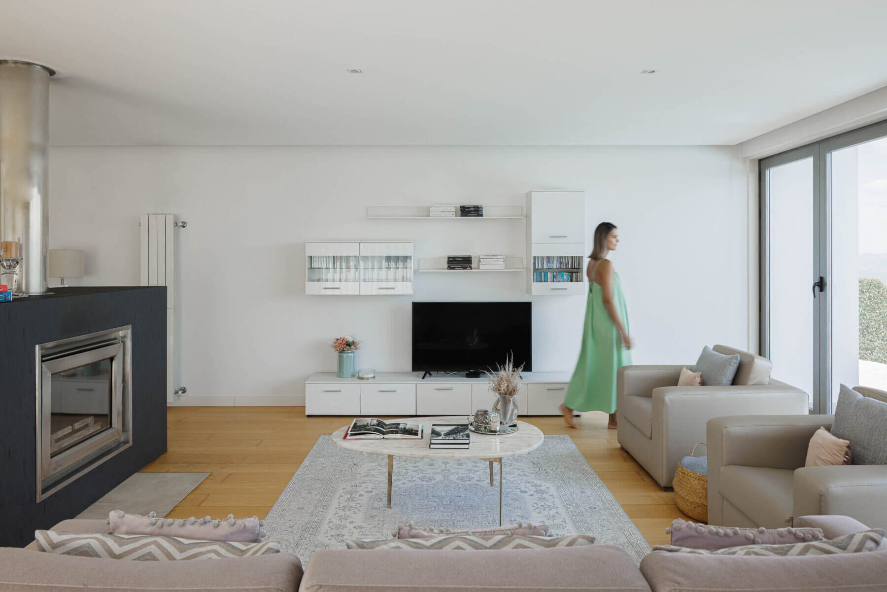 Sala de estar: Lareira moderna, móveis brancos, alcatifa clara e grande janela com vista para o exterior. — Casa do Alto arquitetura Jorge Martins arquiteto em Celorico de Basto
