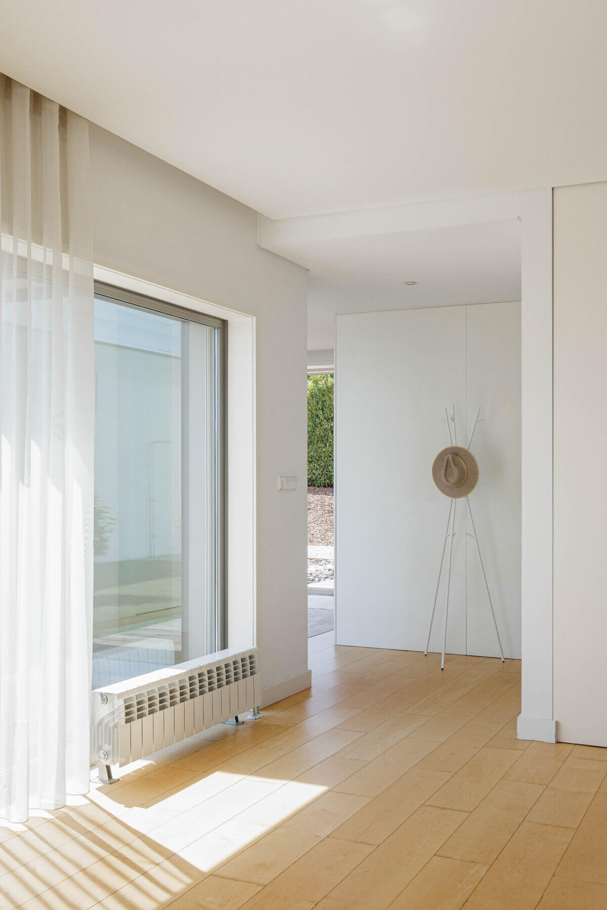Corredor: Pavimento de madeira clara, paredes brancas, radiador e cabideiro minimalista. — Casa do Alto arquitetura Jorge Martins arquiteto em Celorico de Basto