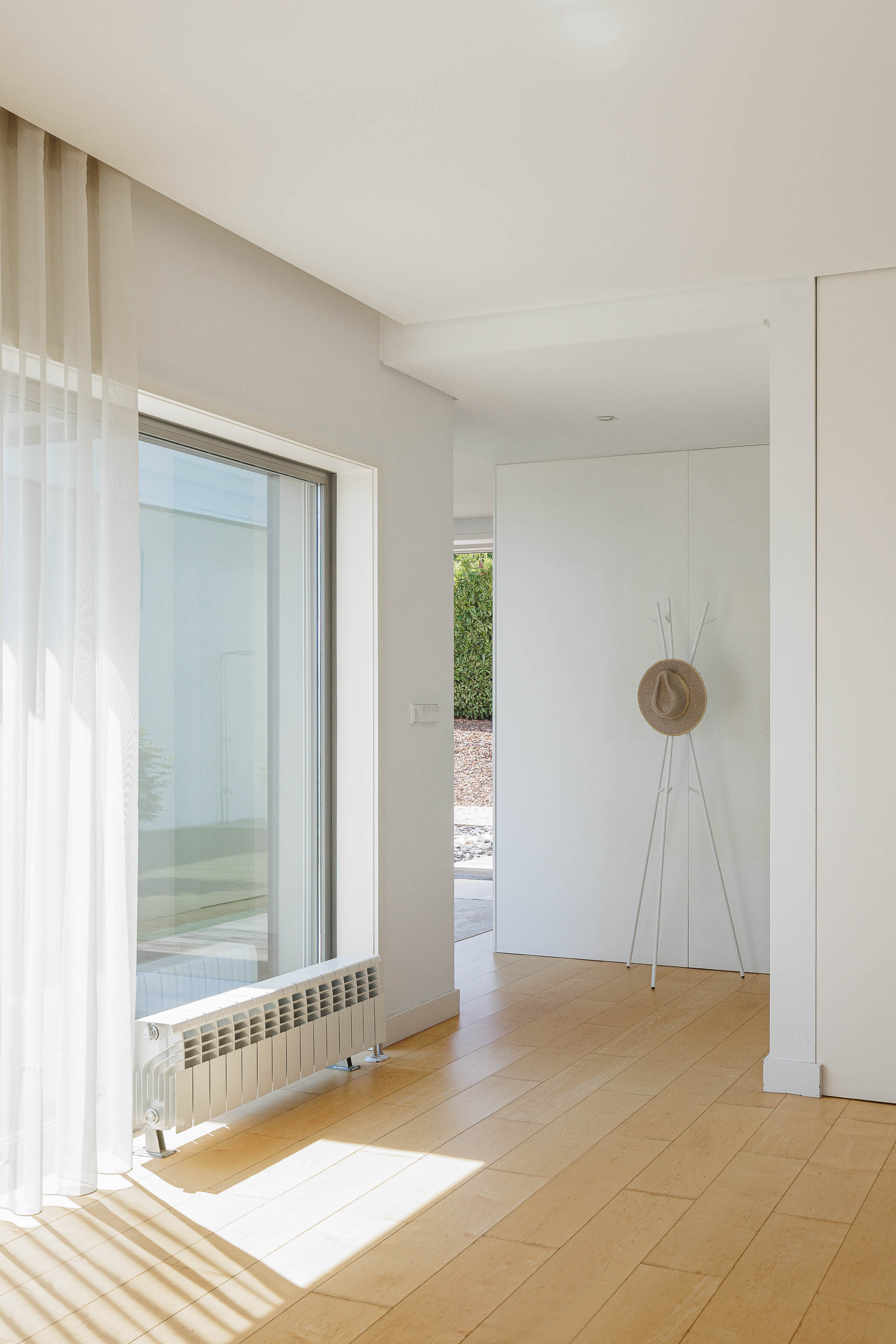 Corredor: Pavimento de madeira clara, paredes brancas, radiador e cabideiro minimalista. — Casa do Alto arquitetura Jorge Martins arquiteto em Celorico de Basto