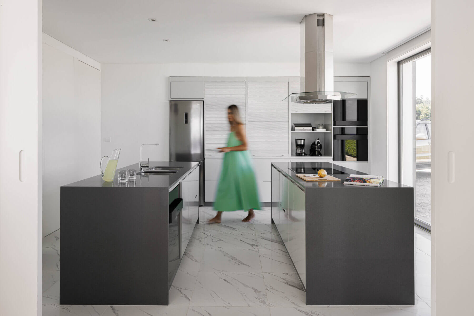 Cozinha: Ilhas centrais com bancadas escuras, armários brancos, pavimento em mármore claro e eletrodomésticos modernos. — Casa do Alto arquitetura Jorge Martins arquiteto em Celorico de Basto