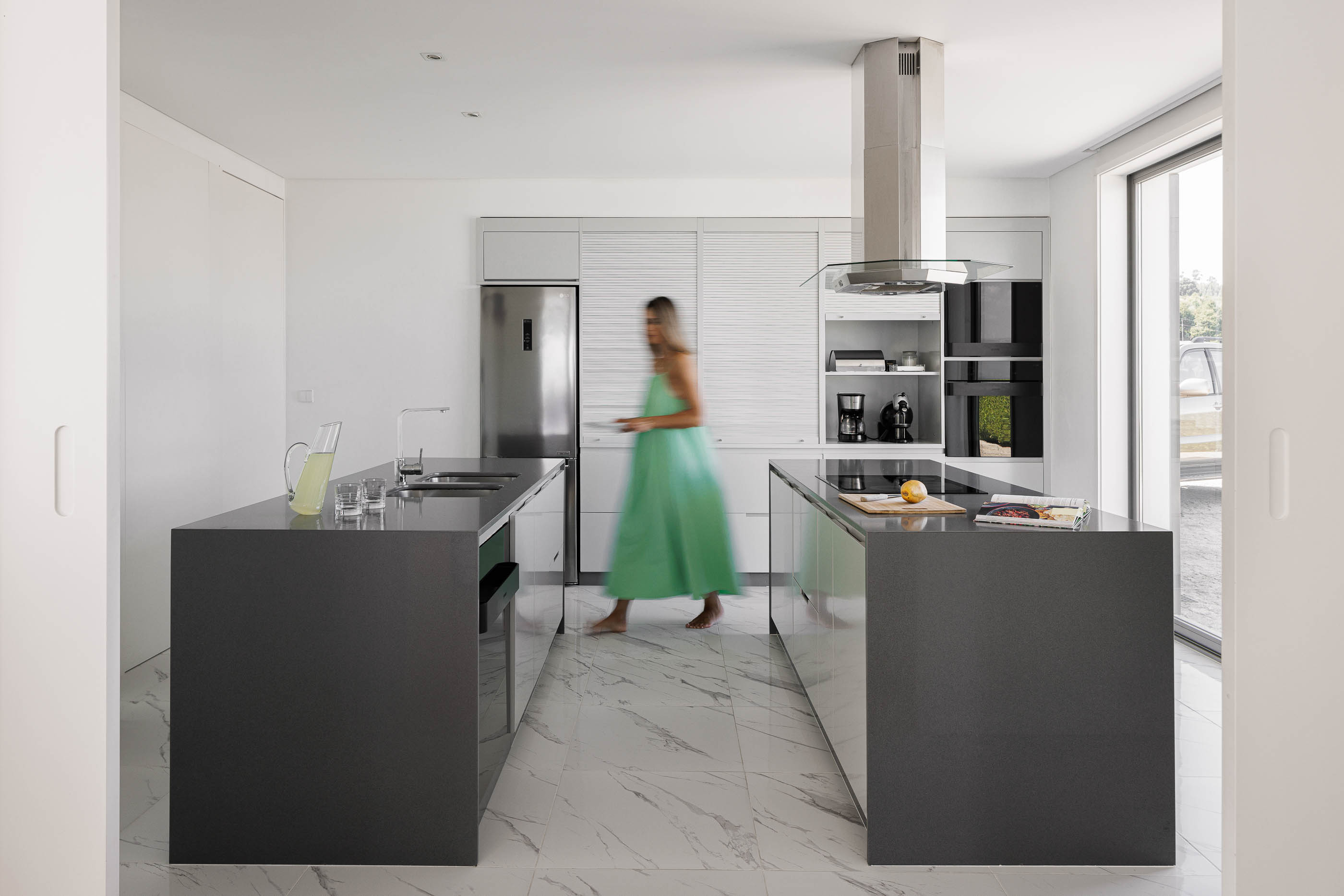 Cozinha: Ilhas centrais com bancadas escuras, armários brancos, pavimento em mármore claro e eletrodomésticos modernos. — Casa do Alto arquitetura Jorge Martins arquiteto em Celorico de Basto
