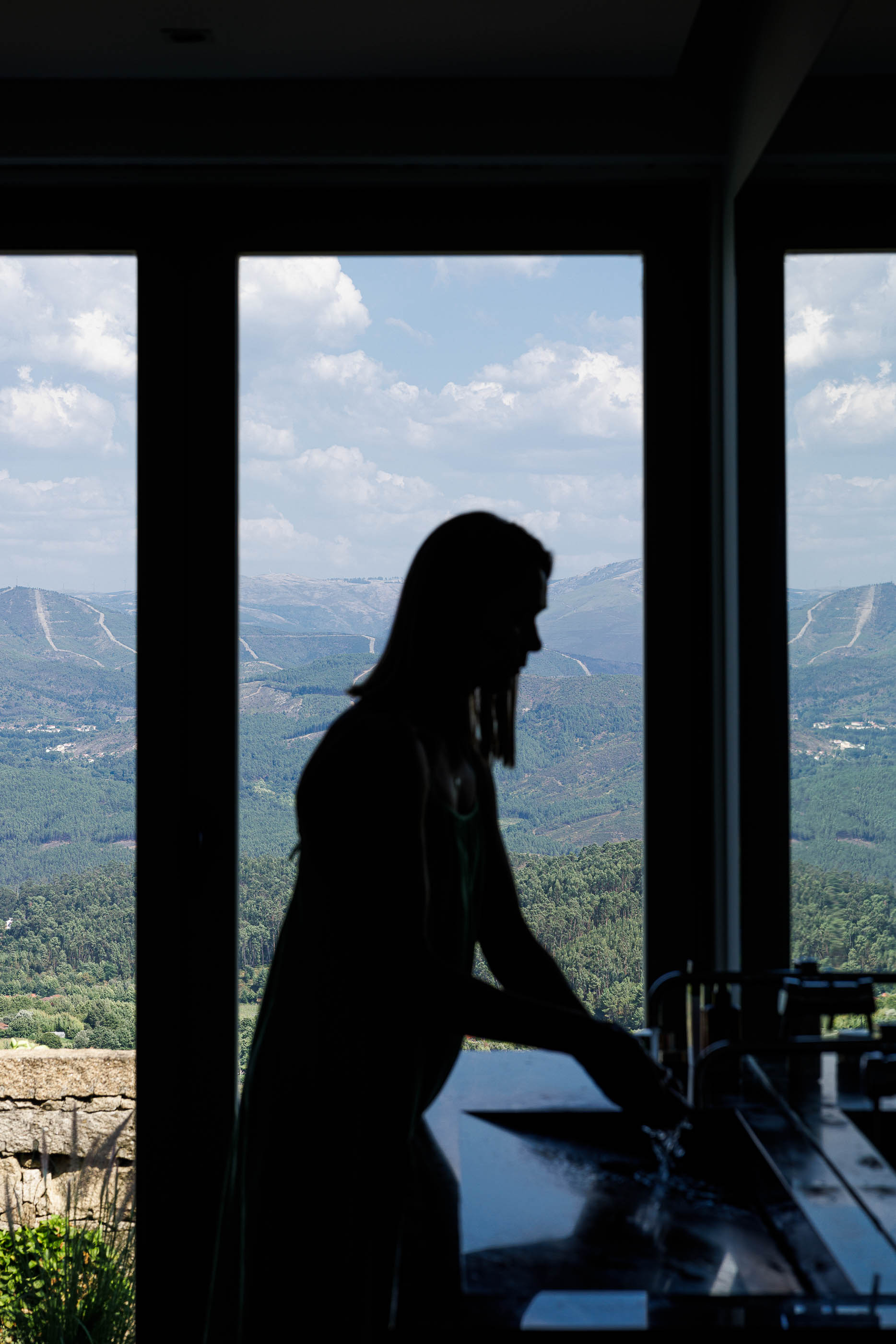 Casa de banho: Silhueta de mulher junto ao lavatório em mármore escuro com vista panorâmica. — Casa do Alto arquitetura Jorge Martins arquiteto em Celorico de Basto