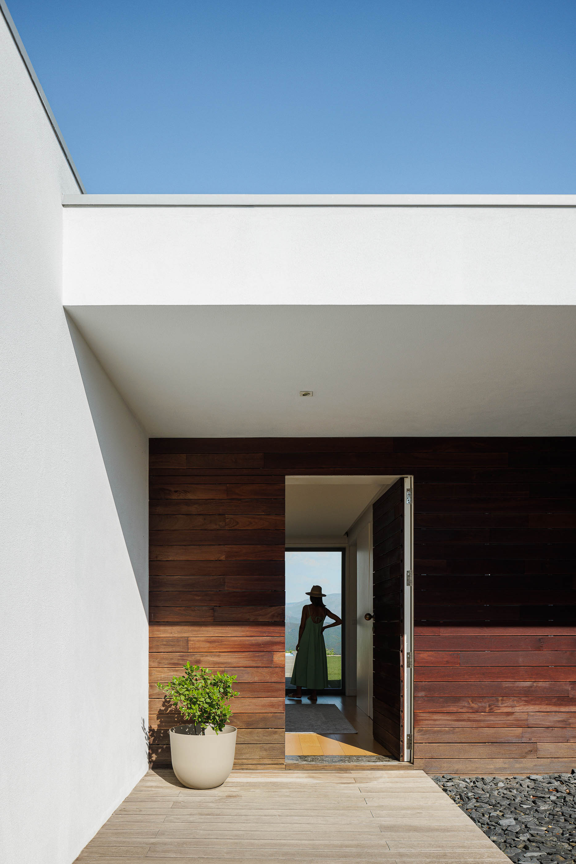 Entrada: Fachada em madeira escura, porta de entrada aberta e pavimento em deck de madeira. — Casa do Alto arquitetura Jorge Martins arquiteto em Celorico de Basto
