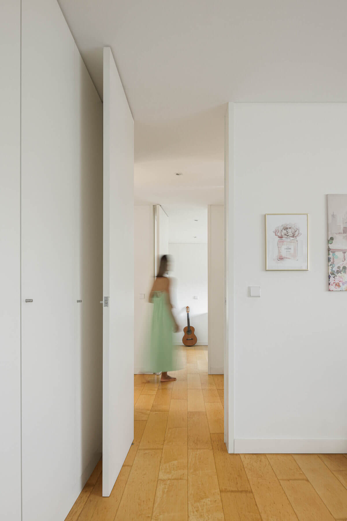 Corredor: Roupeiros embutidos brancos, pavimento de madeira clara e quadros decorativos. — Casa do Alto arquitetura Jorge Martins arquiteto em Celorico de Basto