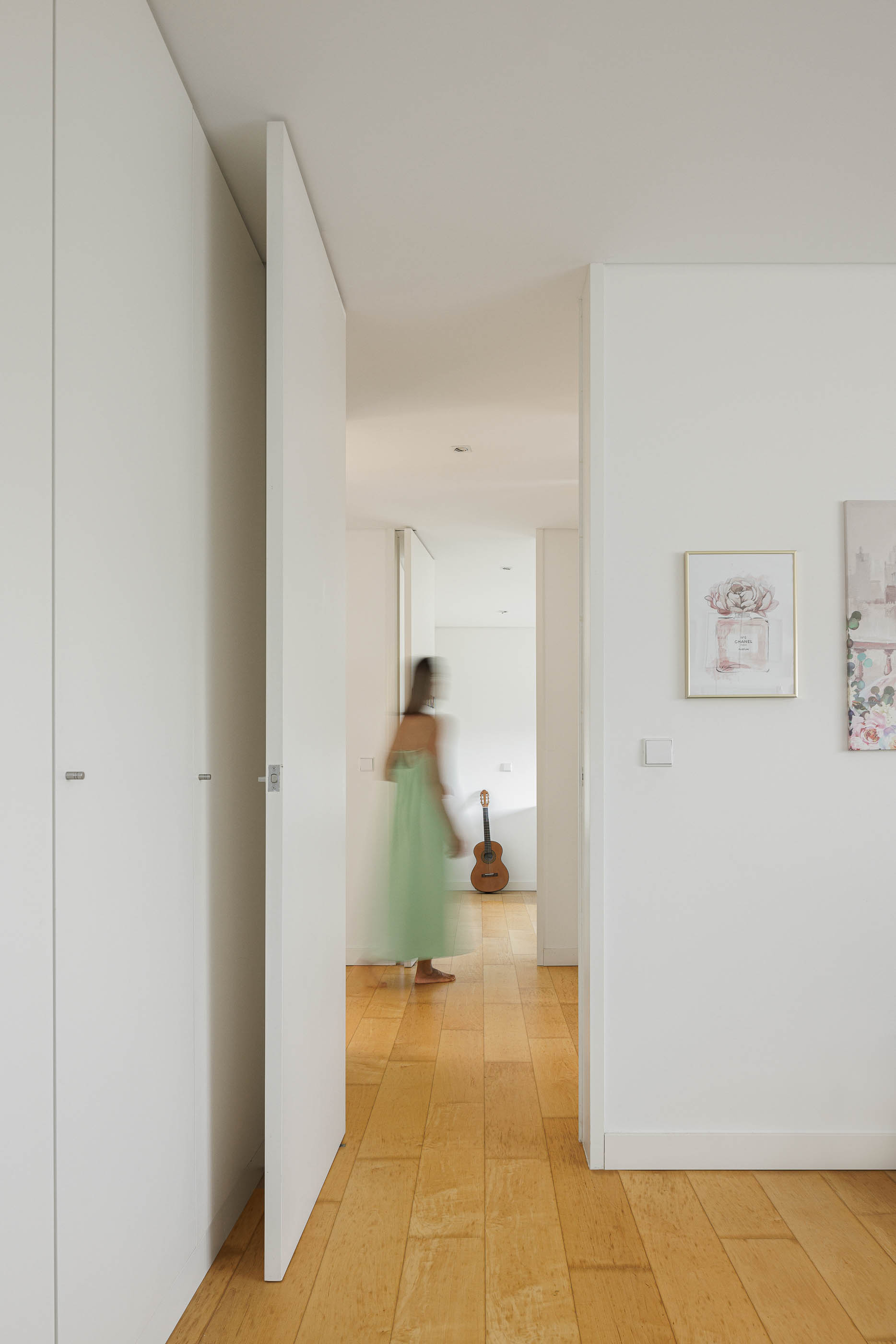 Corredor: Roupeiros embutidos brancos, pavimento de madeira clara e quadros decorativos. — Casa do Alto arquitetura Jorge Martins arquiteto em Celorico de Basto