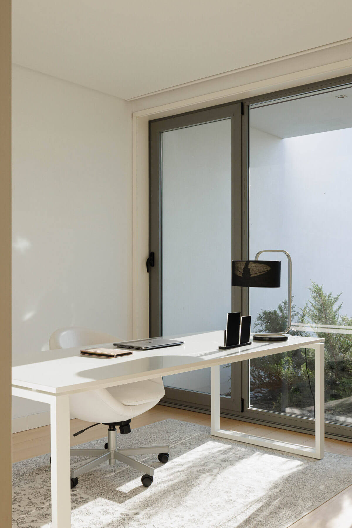 Escritório: Mesa de trabalho branca, cadeira ergonómica e grande janela com vista para o exterior. — Casa do Alto arquitetura Jorge Martins arquiteto em Celorico de Basto