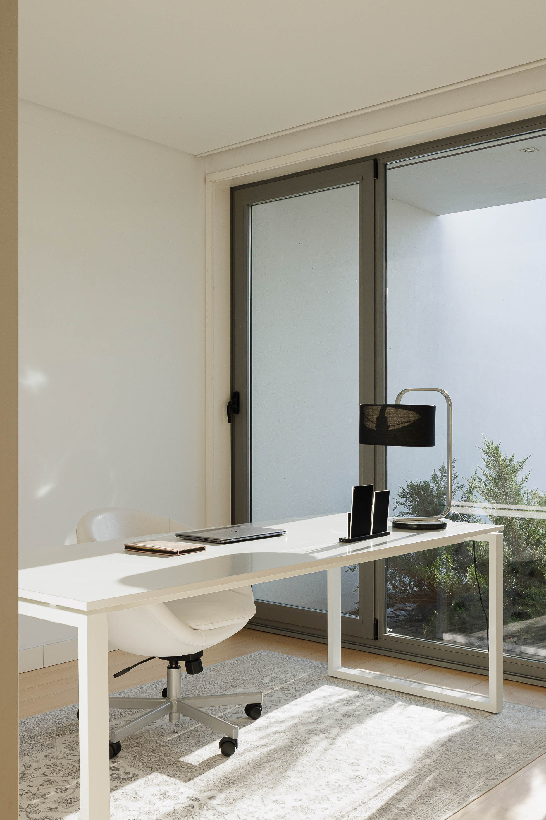 Escritório: Mesa de trabalho branca, cadeira ergonómica e grande janela com vista para o exterior. — Casa do Alto arquitetura Jorge Martins arquiteto em Celorico de Basto