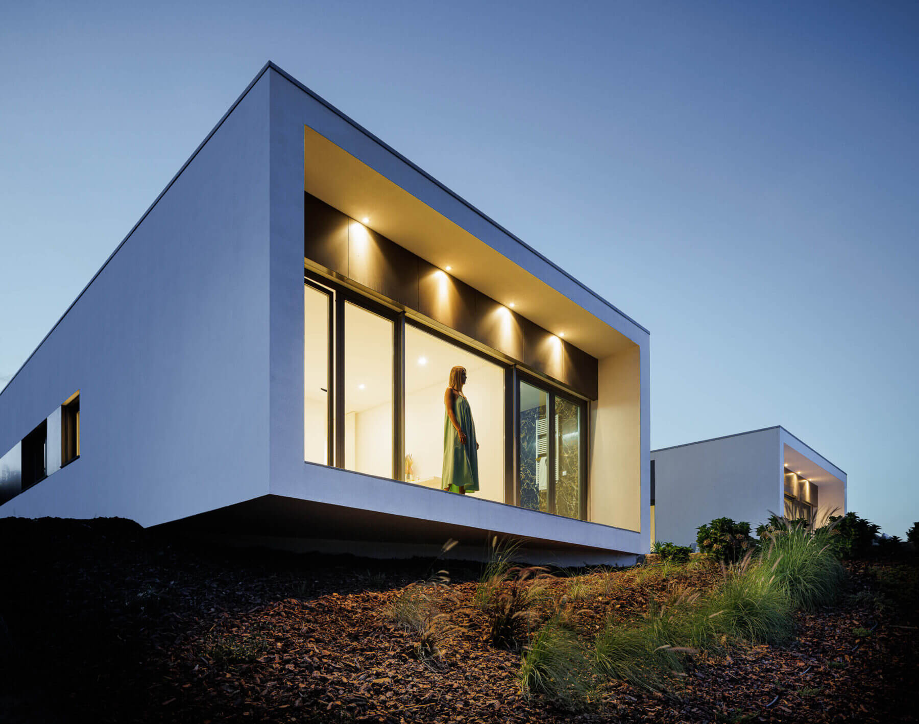 Exterior: Fachada branca iluminada com grandes janelas e paisagem natural. — Casa do Alto arquitetura Jorge Martins arquiteto em Celorico de Basto