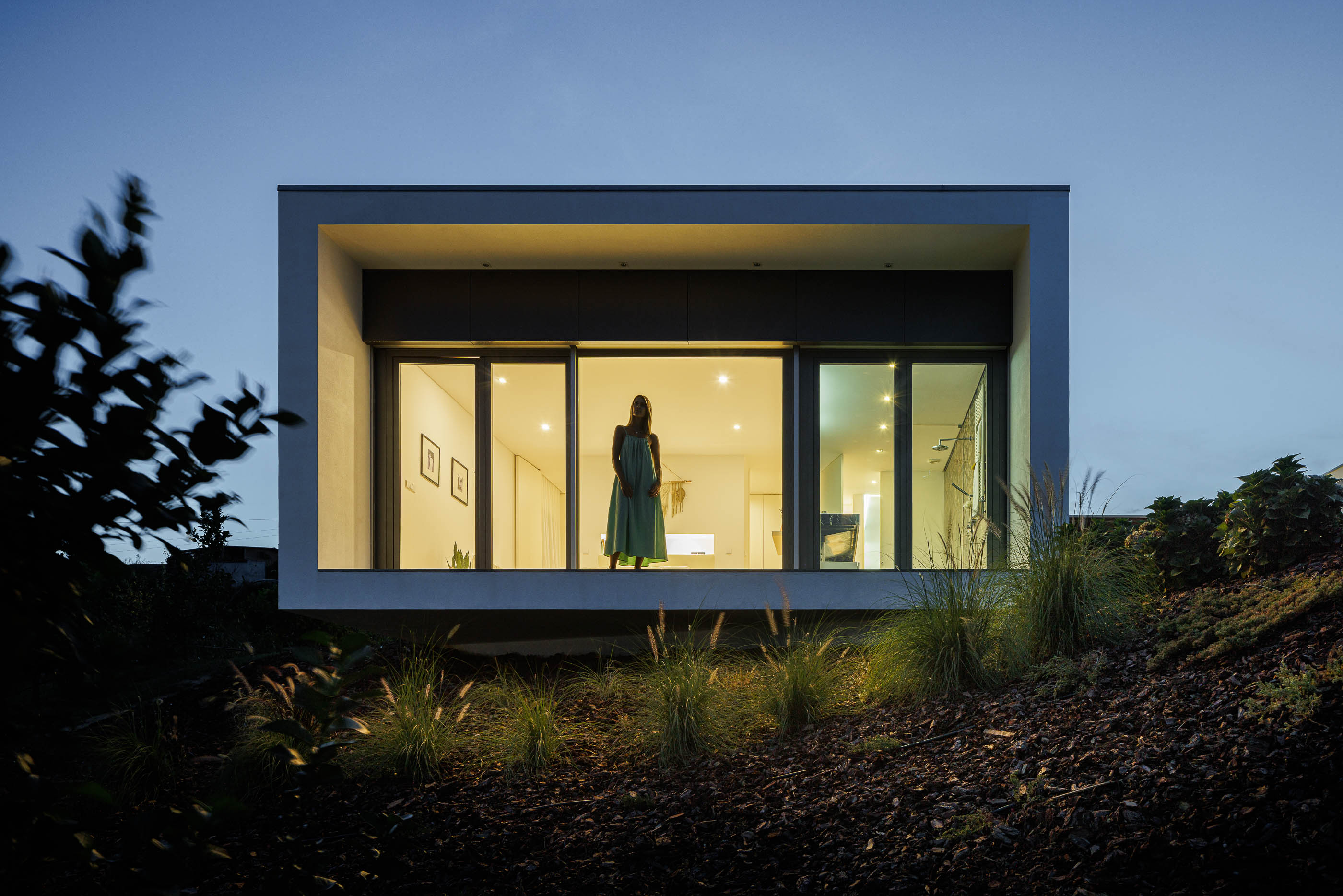Exterior: Fachada branca iluminada com grandes janelas e paisagem natural. — Casa do Alto arquitetura Jorge Martins arquiteto em Celorico de Basto