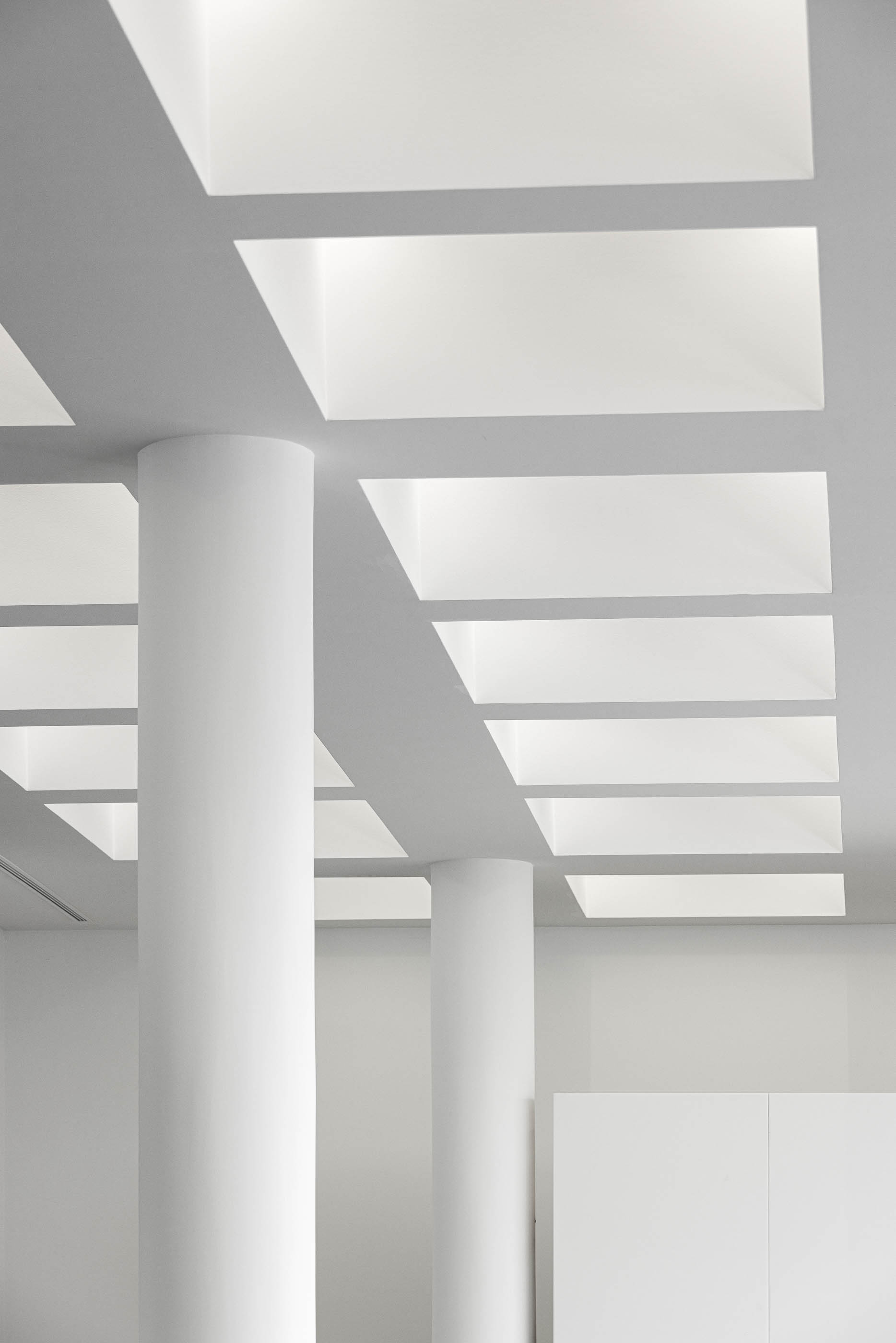 Teto da sala de reuniões com iluminação embutida em grelha e colunas brancas. — Edifício Sede da PRF arquitetura Impare Arquitectura em Leiria