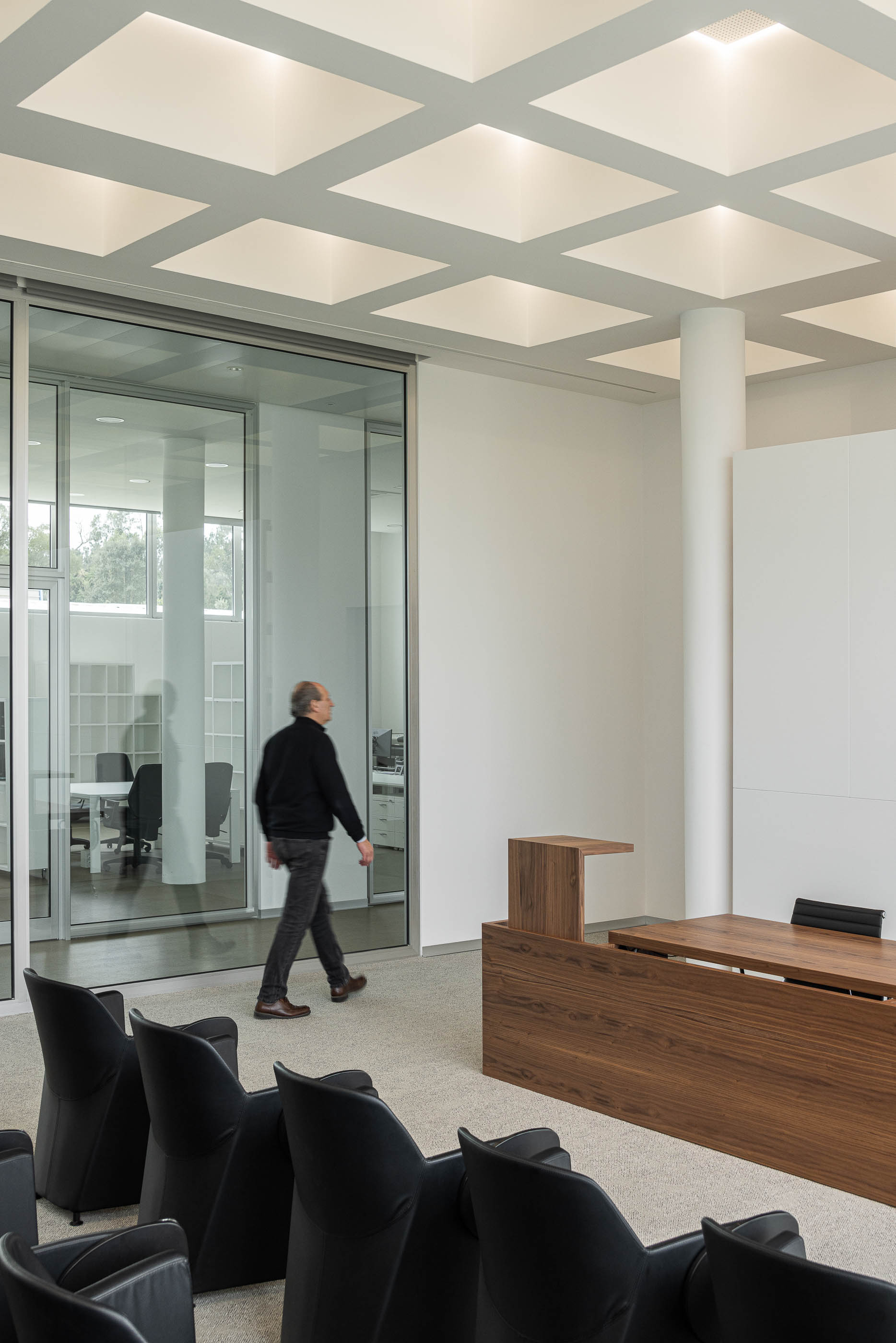 Sala de conferências com cadeiras pretas, mesa de oradores em madeira e pavimento alcatifado cinzento. — Edifício Sede da PRF arquitetura Impare Arquitectura em Leiria