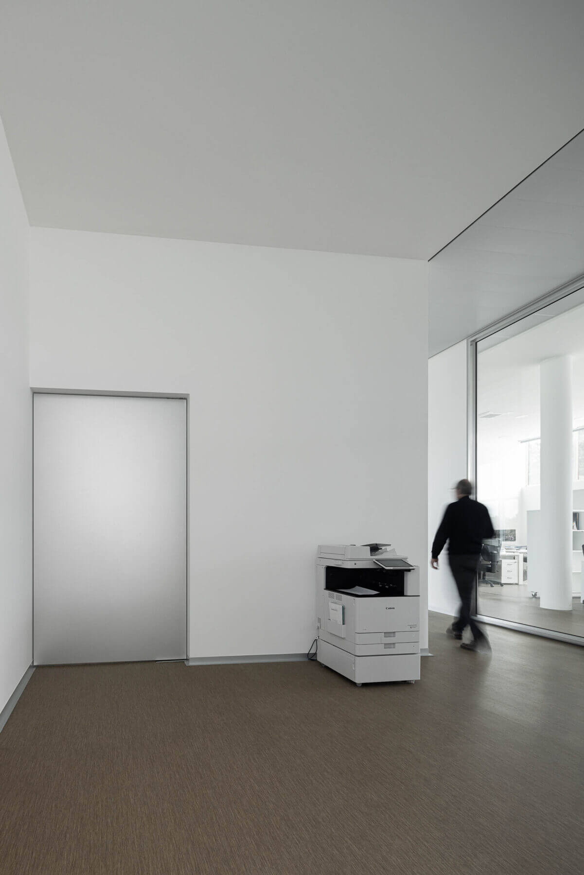 Corredor com pavimento alcatifado castanho, porta branca e máquina de fotocópias. — Edifício Sede da PRF arquitetura Impare Arquitectura em Leiria