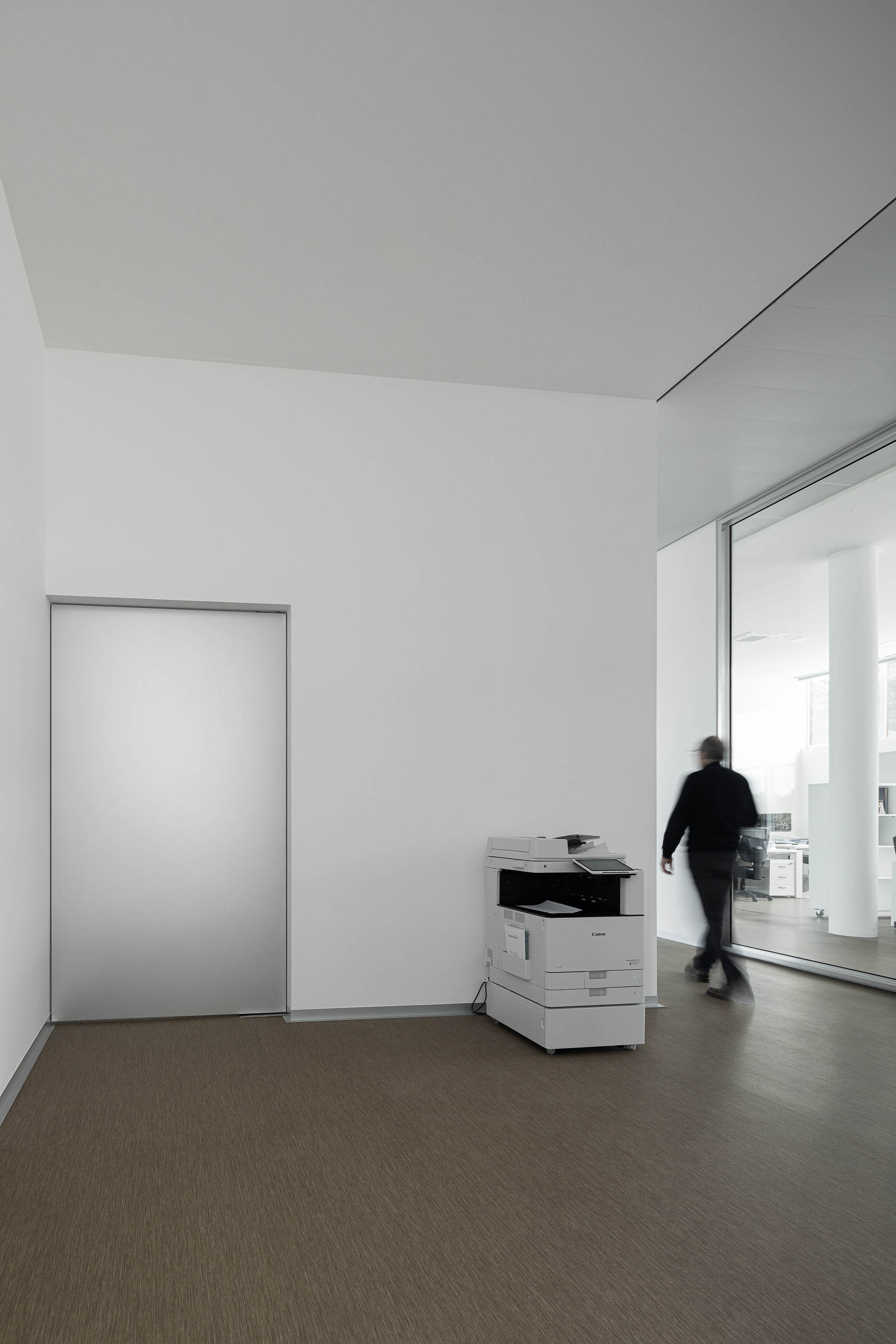 Corredor com pavimento alcatifado castanho, porta branca e máquina de fotocópias. — Edifício Sede da PRF arquitetura Impare Arquitectura em Leiria