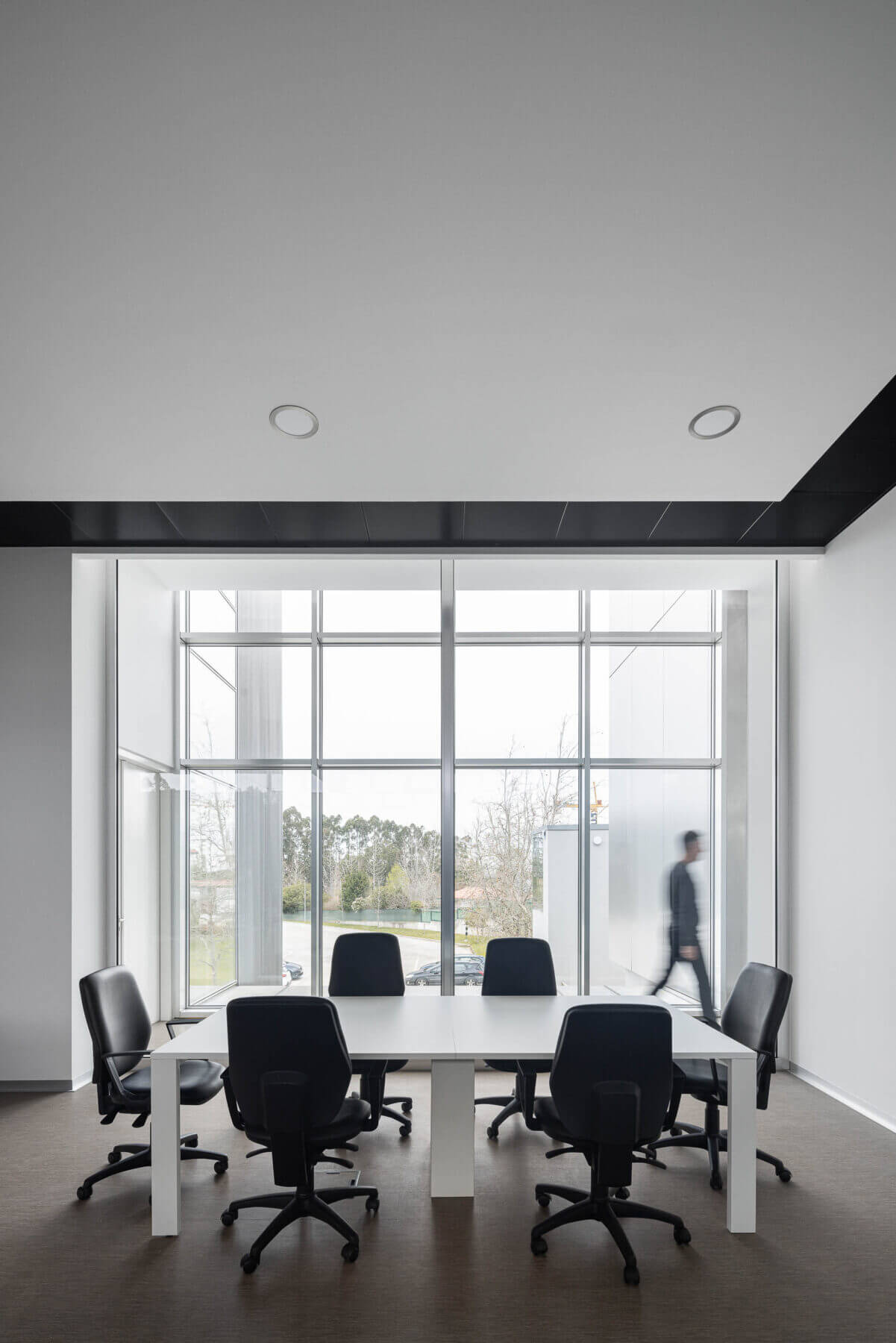 Sala de reuniões com mesa branca, cadeiras pretas e grande janela com vista para o exterior. — Edifício Sede da PRF arquitetura Impare Arquitectura em Leiria