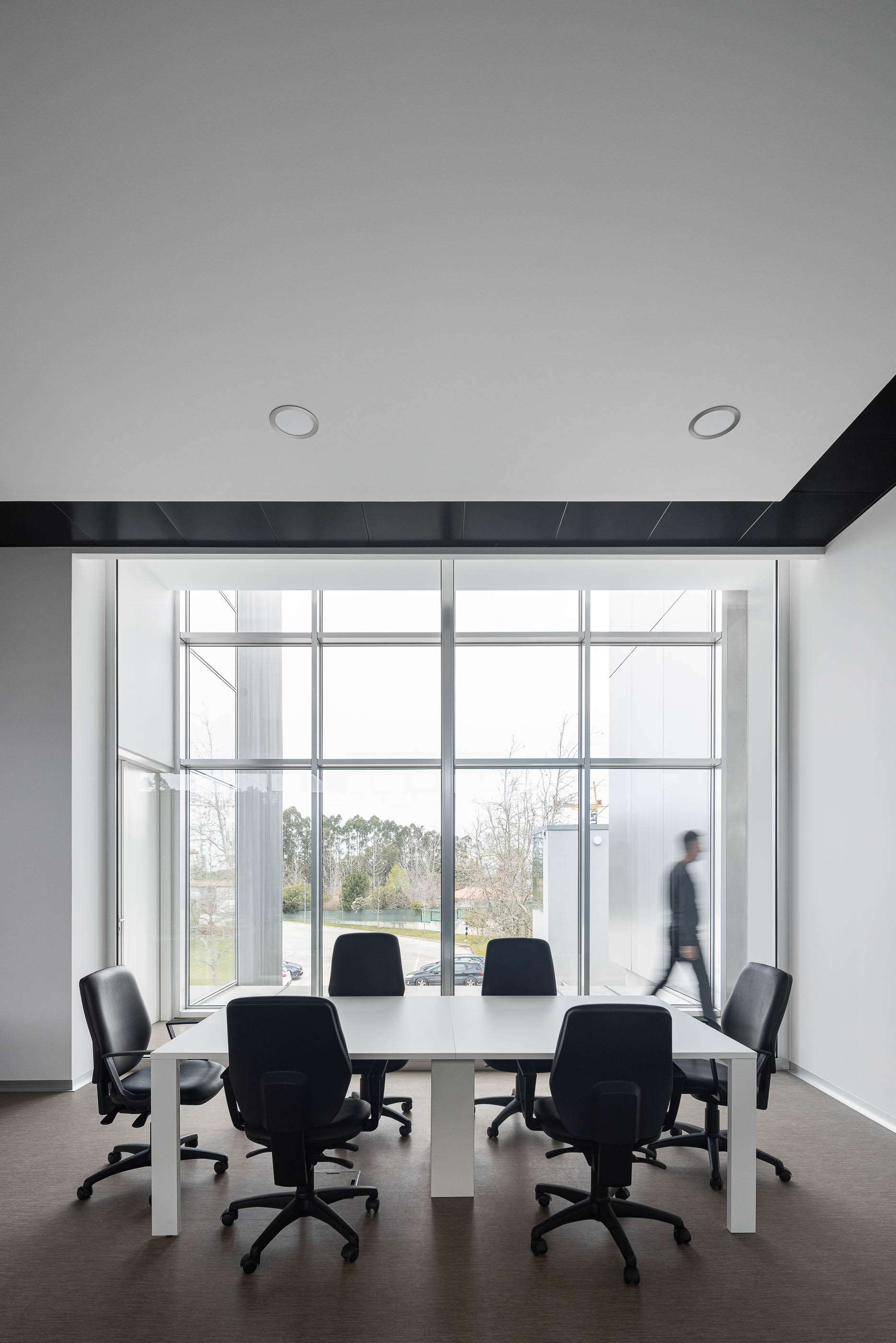 Sala de reuniões com mesa branca, cadeiras pretas e grande janela com vista para o exterior. — Edifício Sede da PRF arquitetura Impare Arquitectura em Leiria