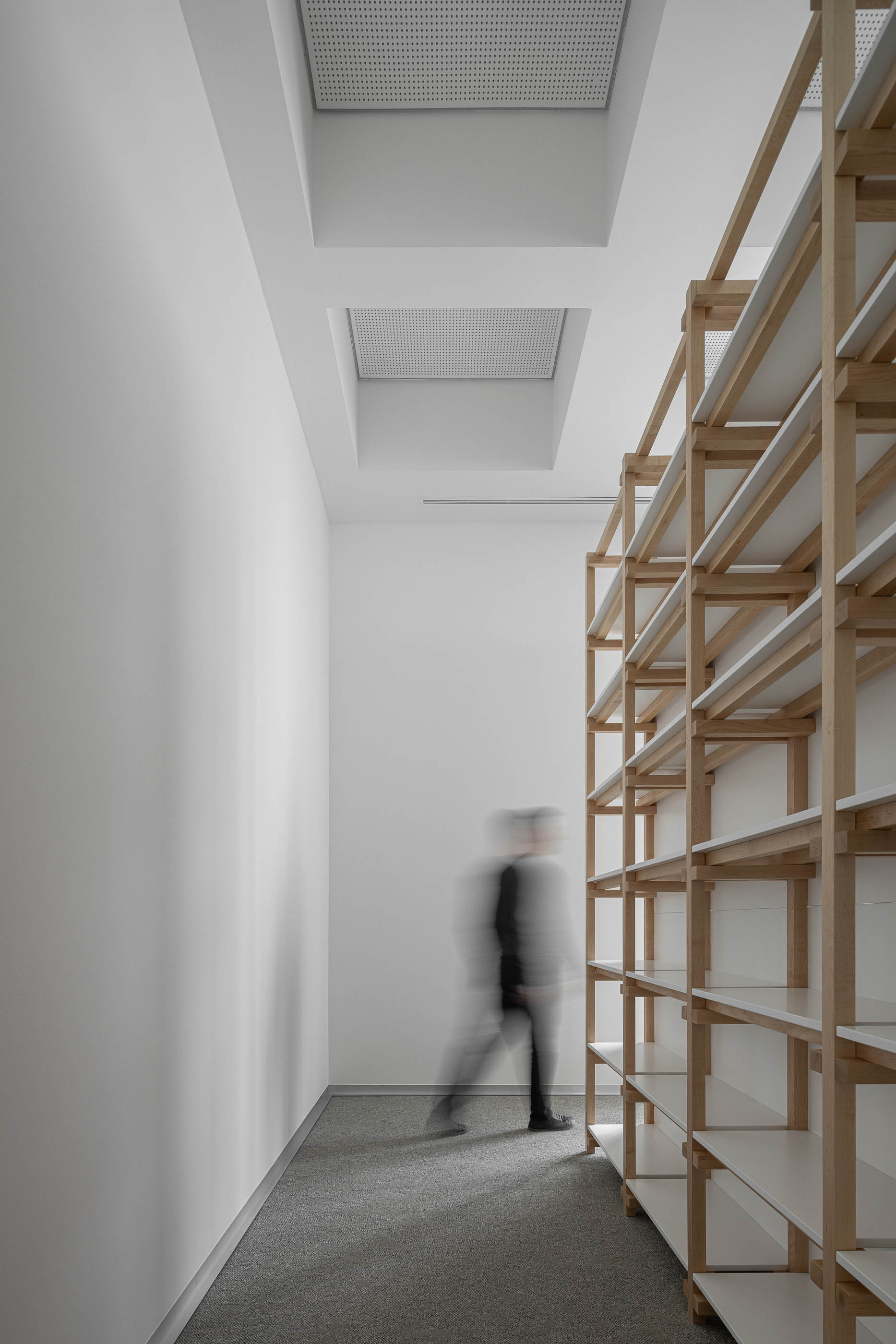 Arquivo com estantes de madeira clara e prateleiras brancas. Pavimento alcatifado cinzento. — Edifício Sede da PRF arquitetura Impare Arquitectura em Leiria