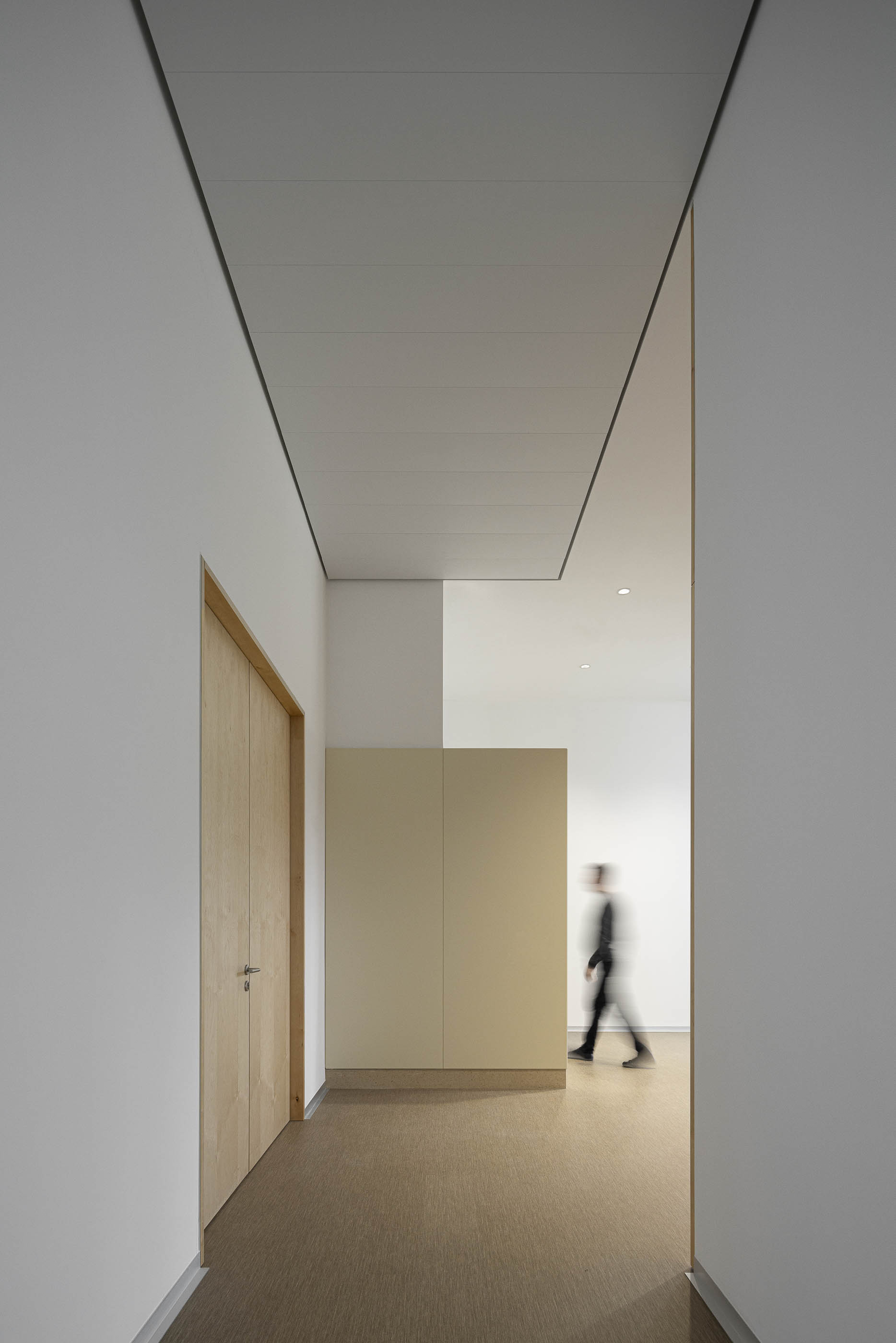 Corredor com paredes brancas e portas de madeira clara. Pavimento em tons de bege. — Edifício Sede da PRF arquitetura Impare Arquitectura em Leiria
