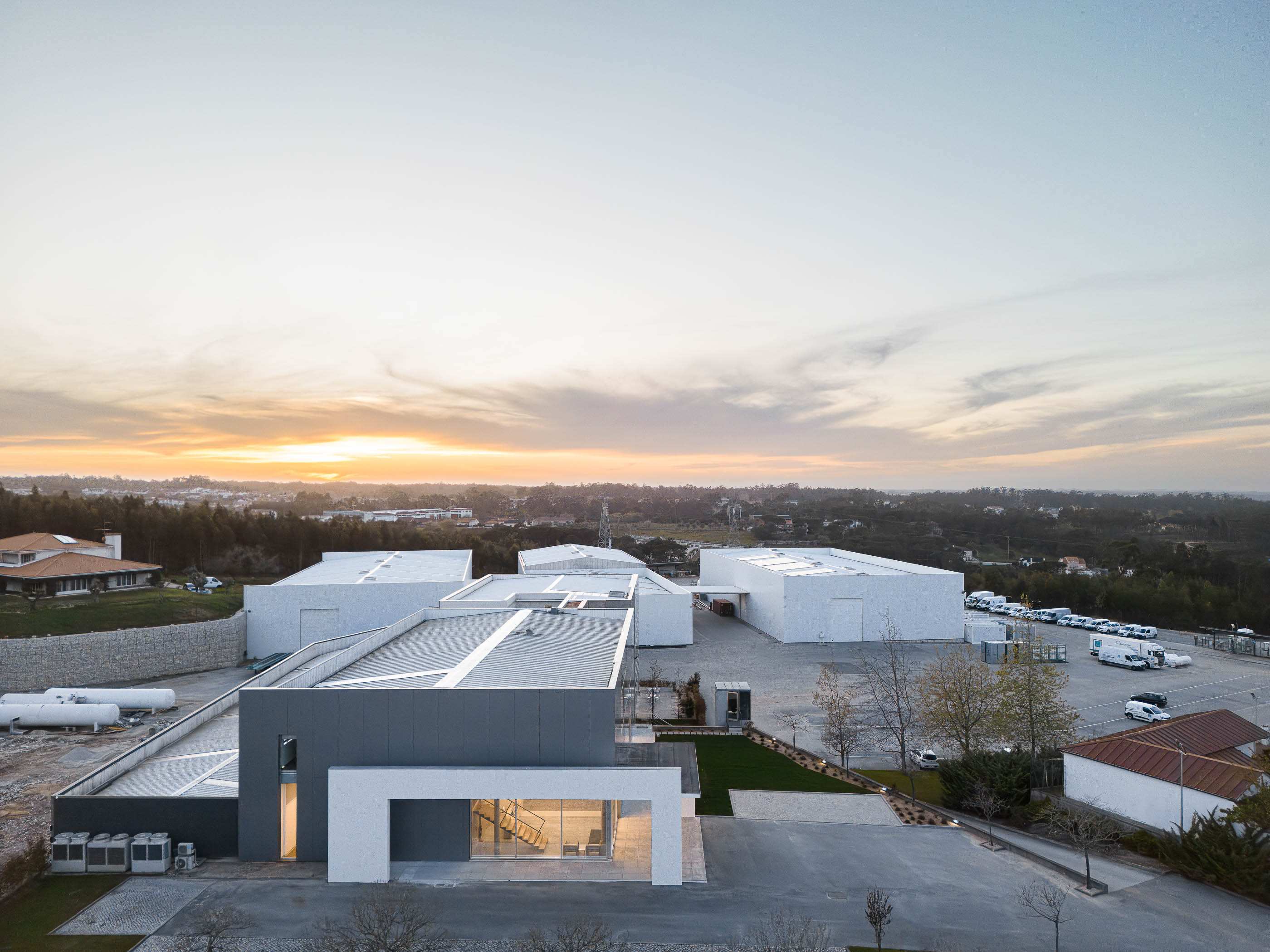 Vista aérea do edifício com telhados brancos e cinzentos ao pôr do sol. — Edifício Sede da PRF arquitetura Impare Arquitectura em Leiria