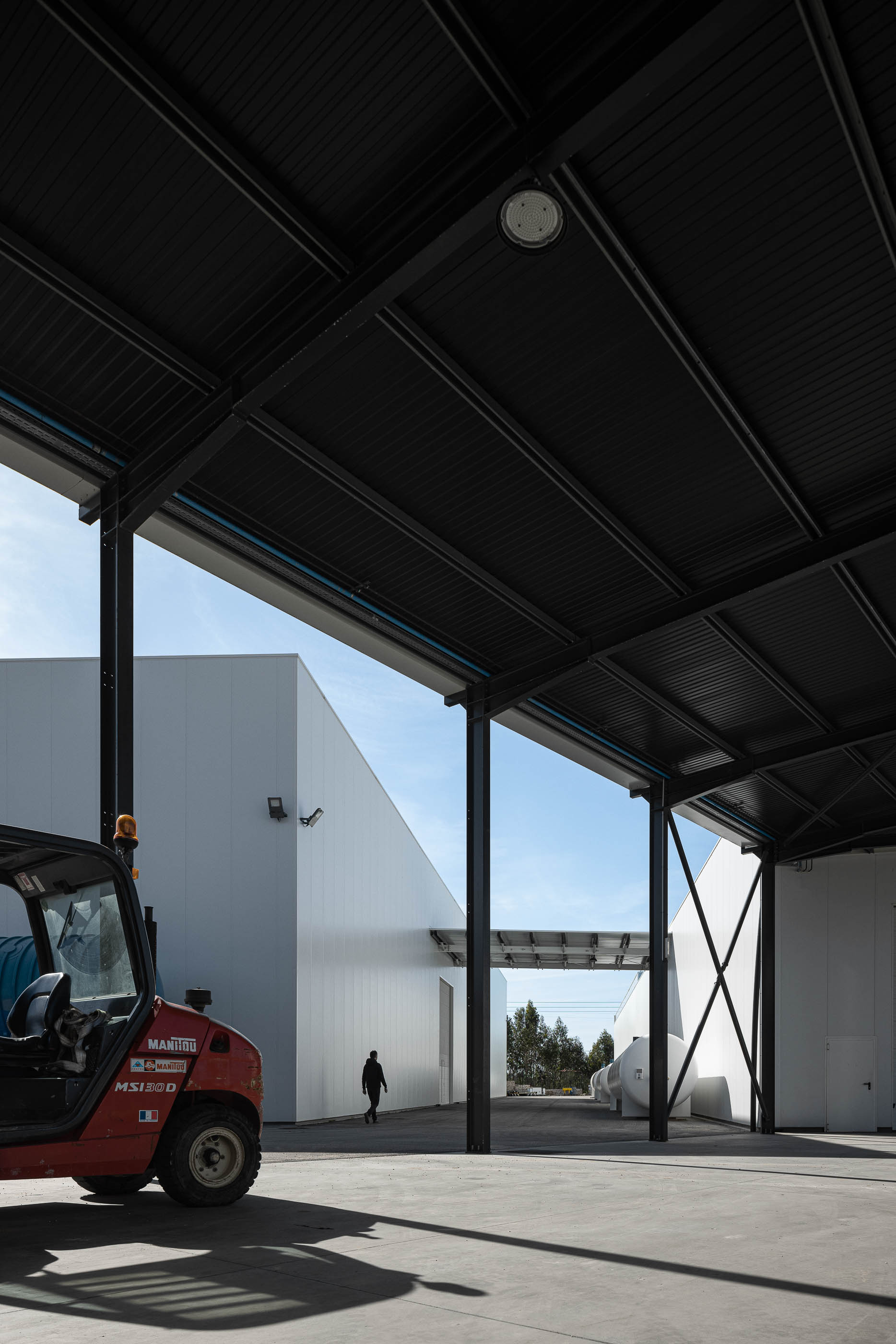 Armazém com estrutura metálica preta e empilhadora vermelha. — Edifício Sede da PRF arquitetura Impare Arquitectura em Leiria
