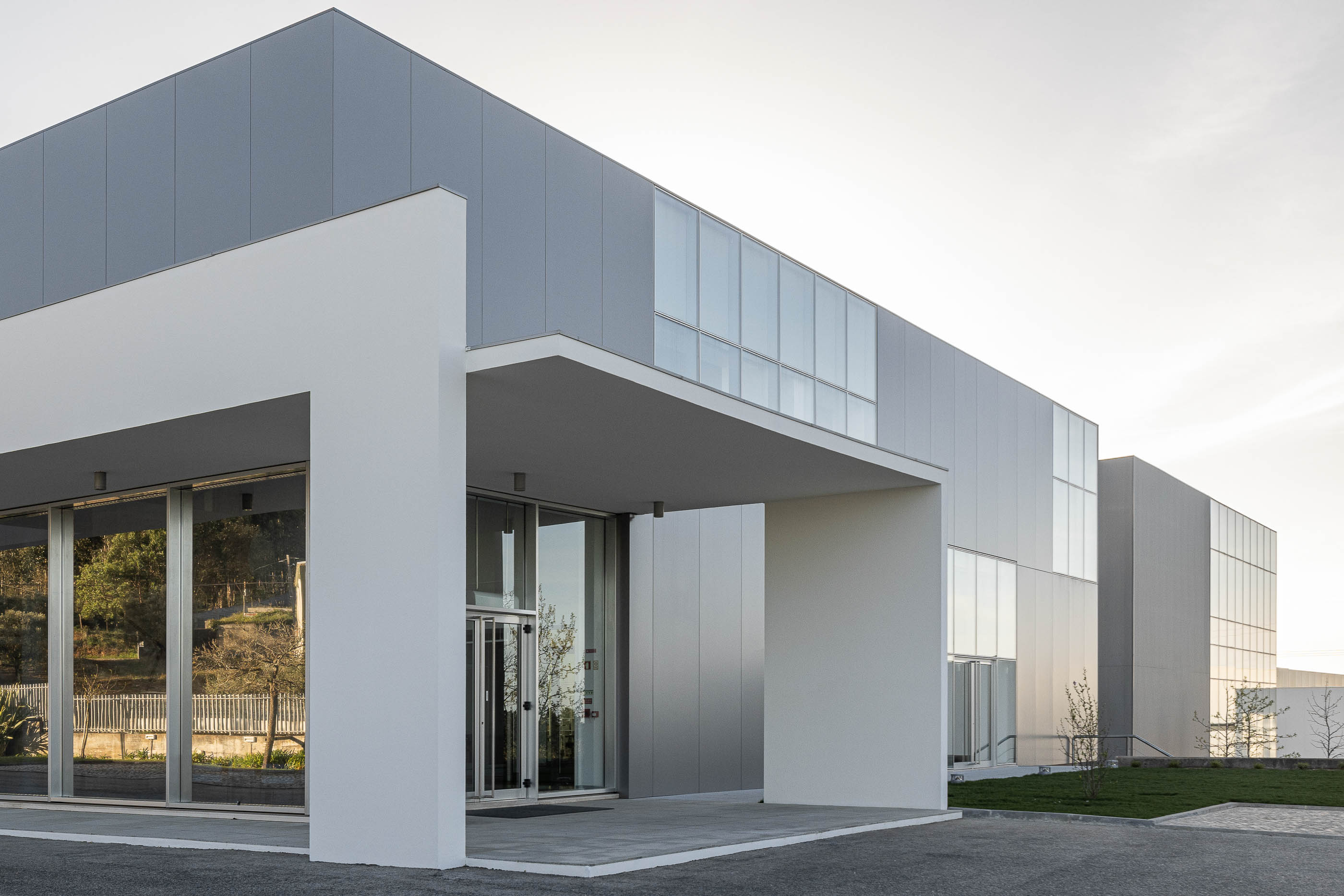 Fachada principal do edifício com entrada envidraçada e estrutura branca. — Edifício Sede da PRF arquitetura Impare Arquitectura em Leiria