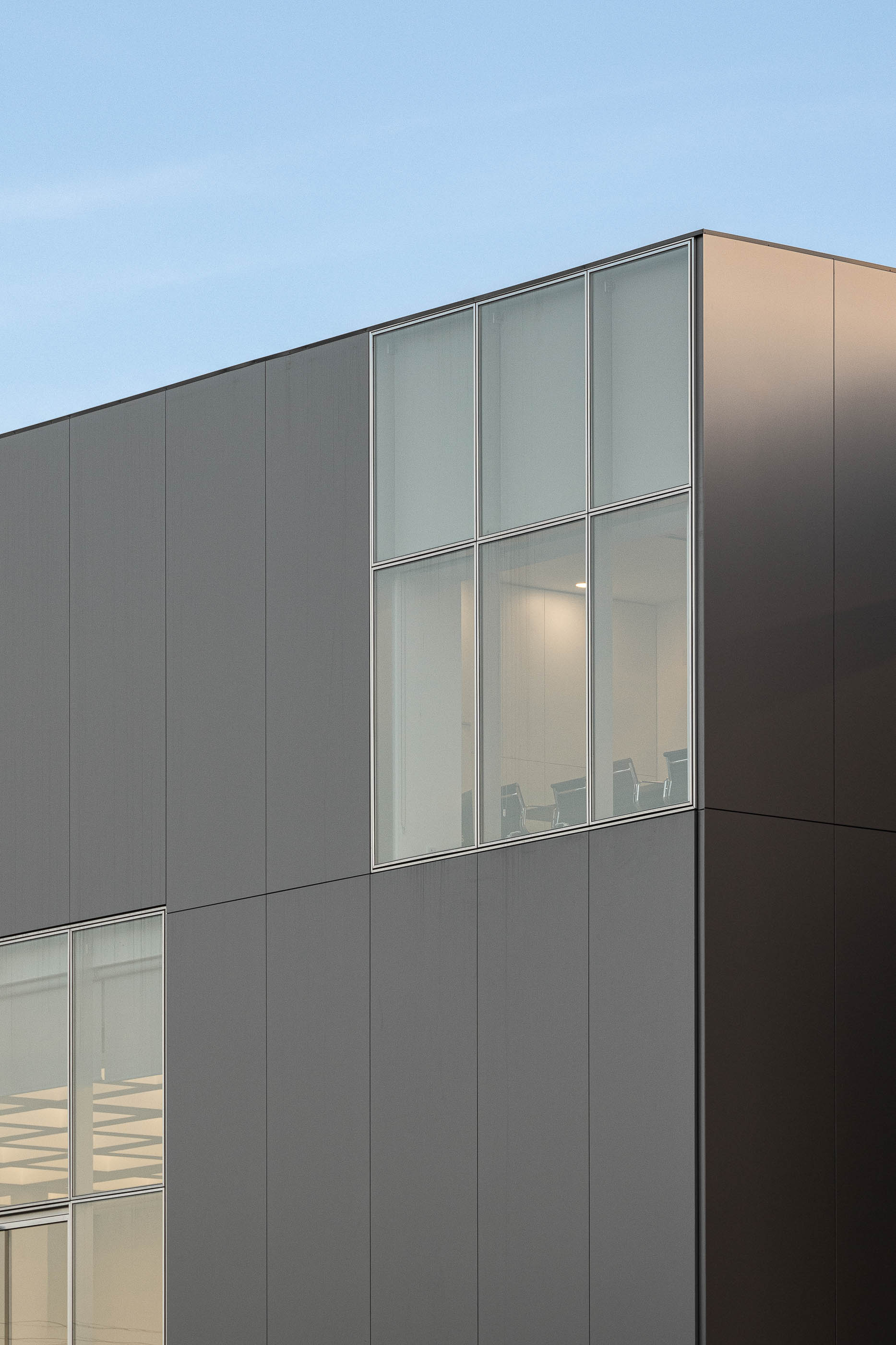 Detalhe da fachada cinzenta com janelas e vista para o interior. — Edifício Sede da PRF arquitetura Impare Arquitectura em Leiria