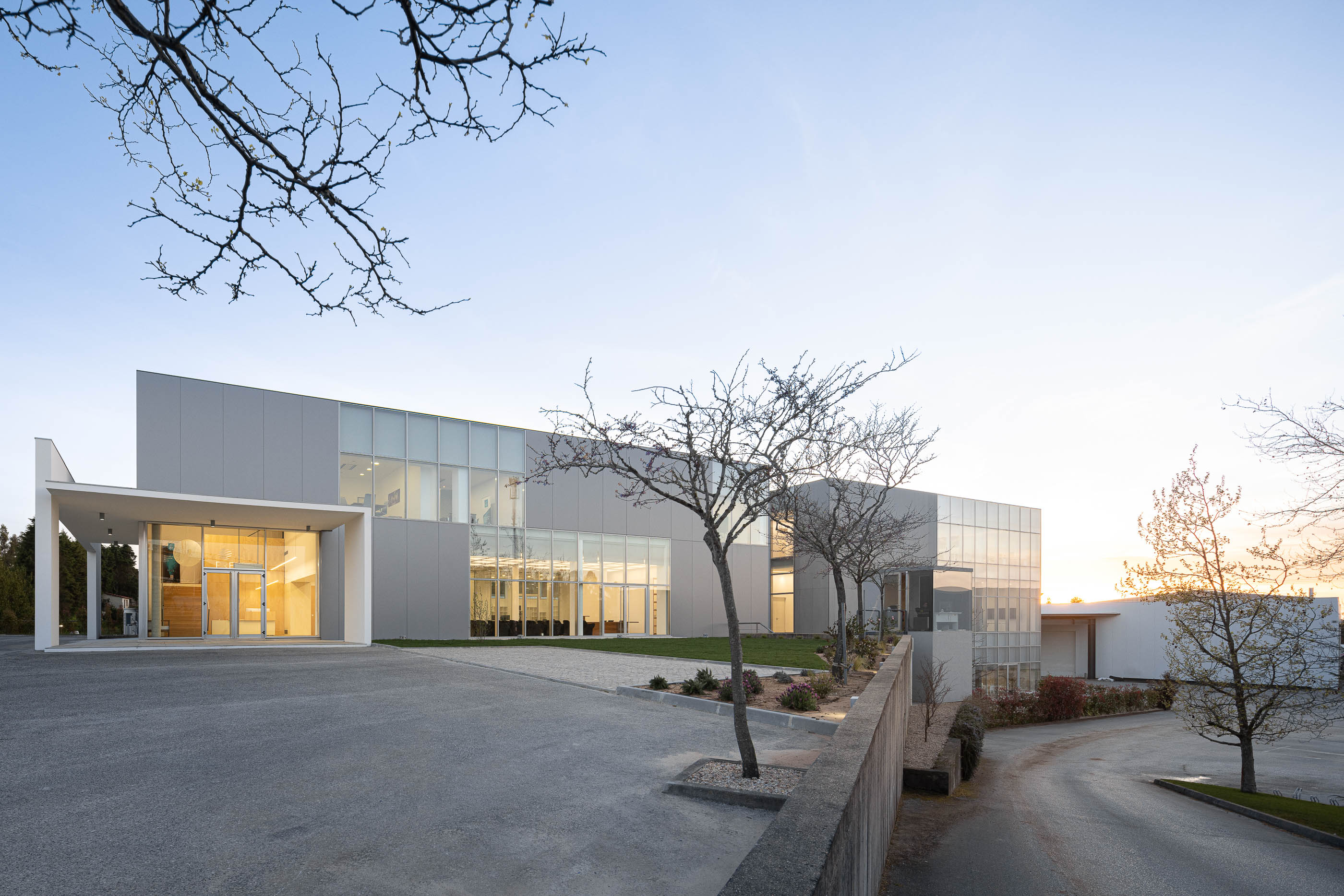 Fachada principal do edifício com entrada envidraçada e estacionamento. — Edifício Sede da PRF arquitetura Impare Arquitectura em Leiria