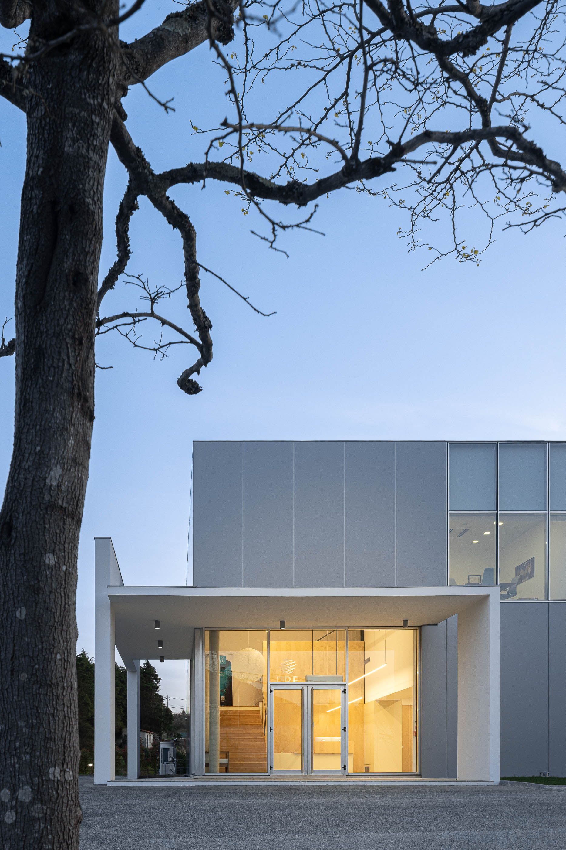 Fachada principal do edifício com entrada envidraçada e iluminação exterior. — Edifício Sede da PRF arquitetura Impare Arquitectura em Leiria