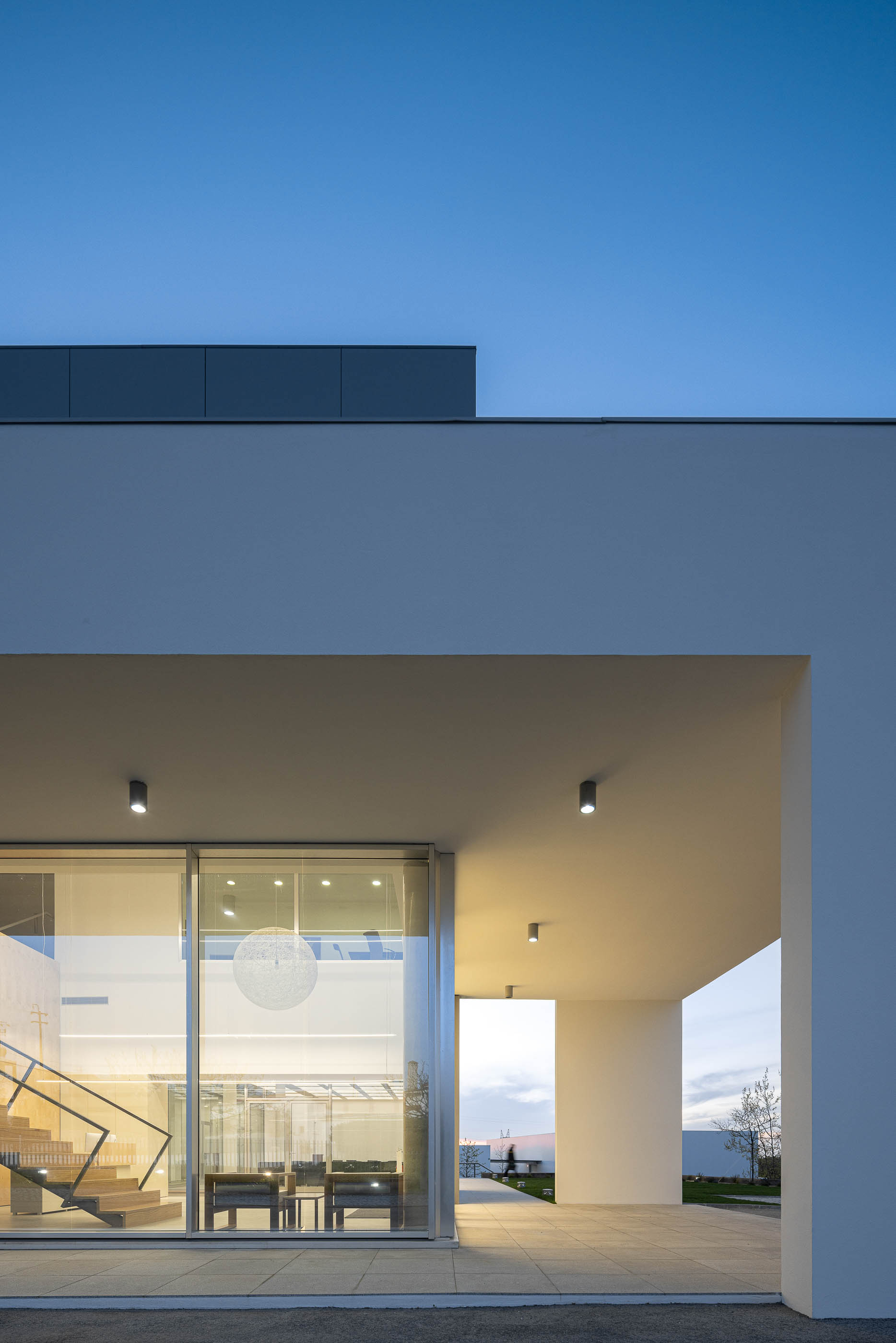 Fachada envidraçada da sala de conferências com cadeiras pretas e iluminação interior. — Edifício Sede da PRF arquitetura Impare Arquitectura em Leiria