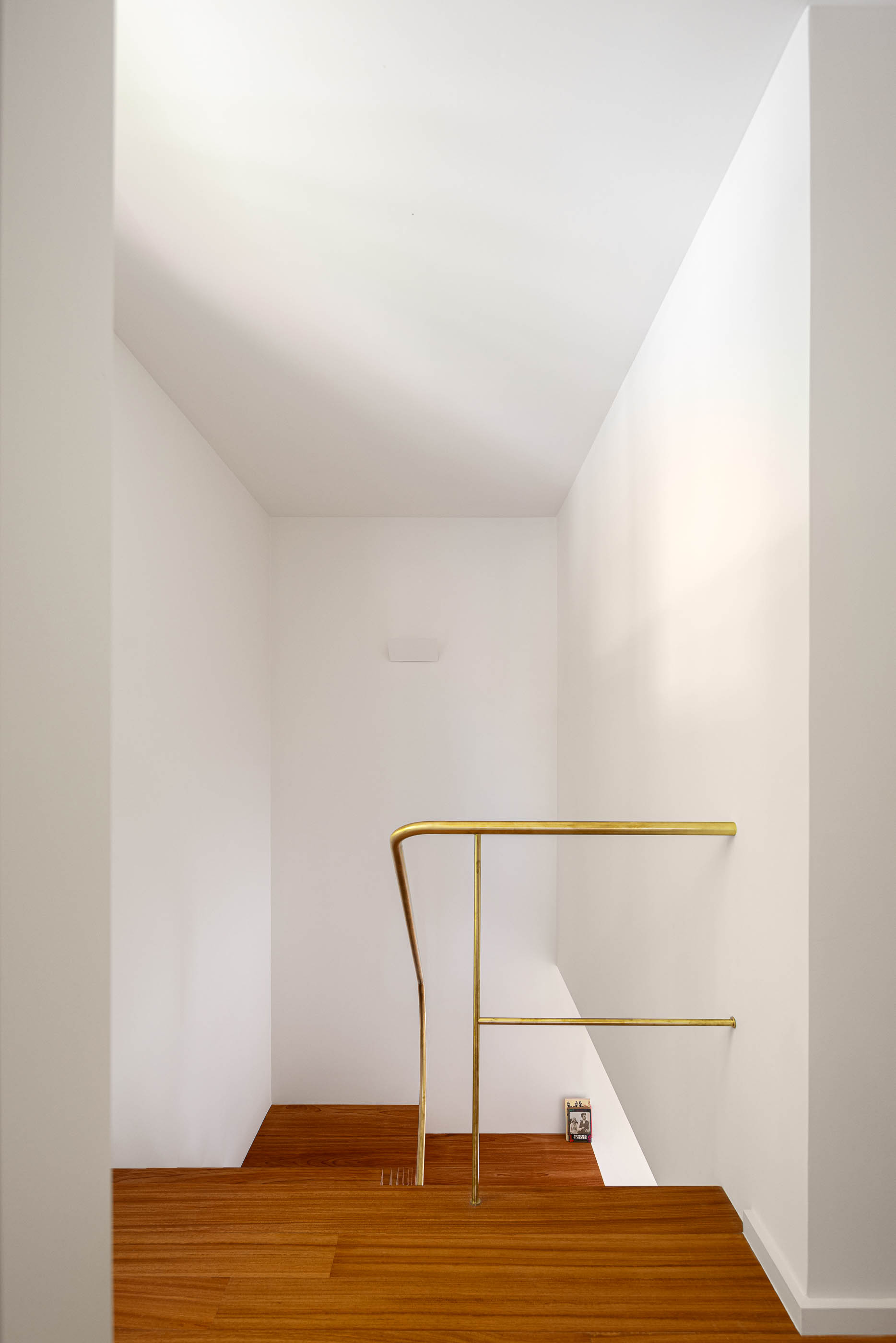 Escadas: Corrimão dourado e degraus em madeira clara, com paredes brancas. — Casa IMLA arquitetura Luppa em Porto