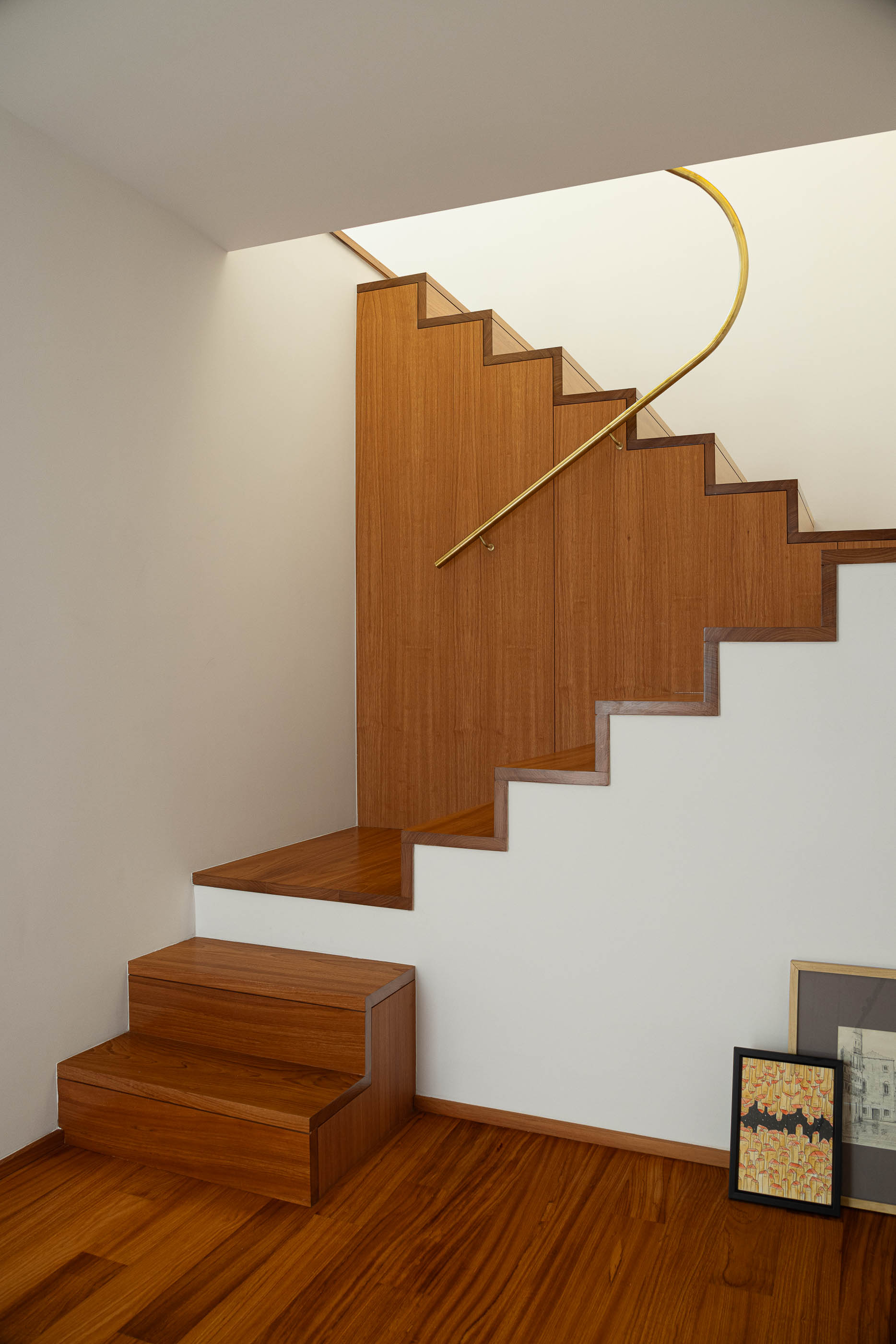 Escadas: Degraus em madeira clara, corrimão dourado curvo e pavimento em madeira. — Casa IMLA arquitetura Luppa em Porto