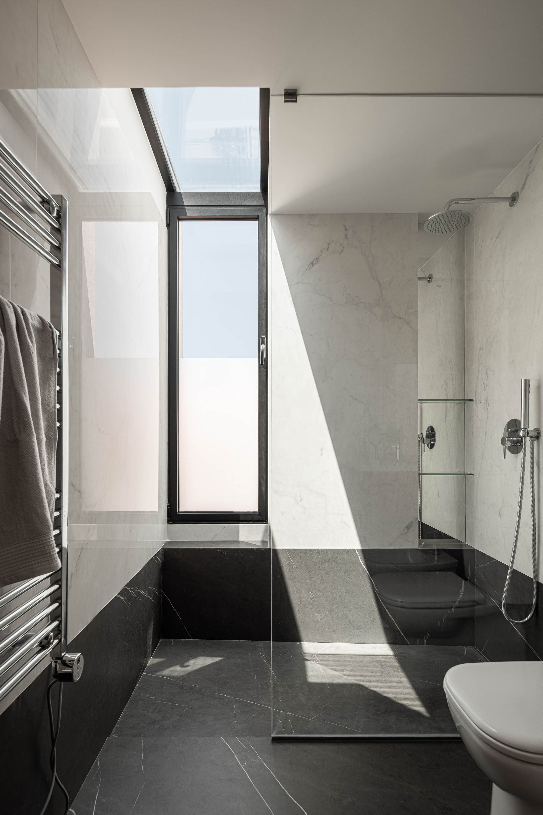 Casa de banho: Cabine de duche em mármore branco com claraboia, pavimento em mármore preto e toalheiro aquecido. — Casa IMLA arquitetura Luppa em Porto