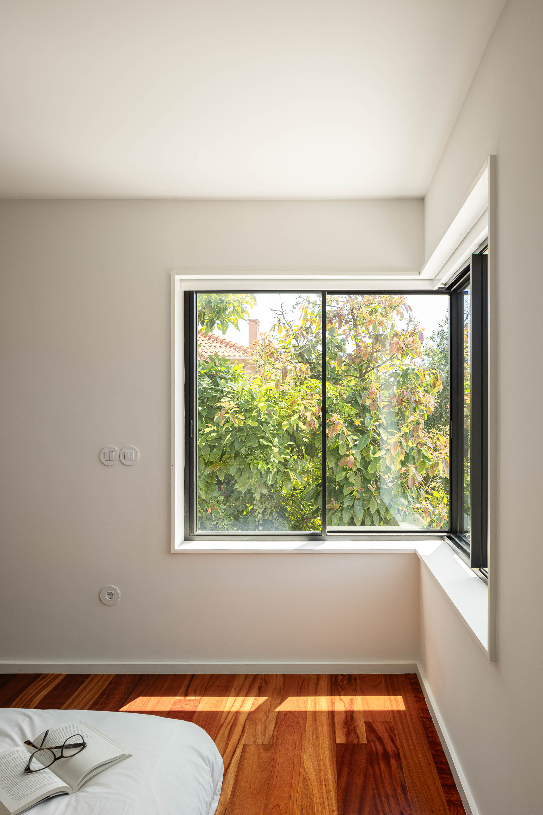 Quarto: Canto com janela ampla, pavimento em madeira e roupa de cama branca. — Casa IMLA arquitetura Luppa em Porto