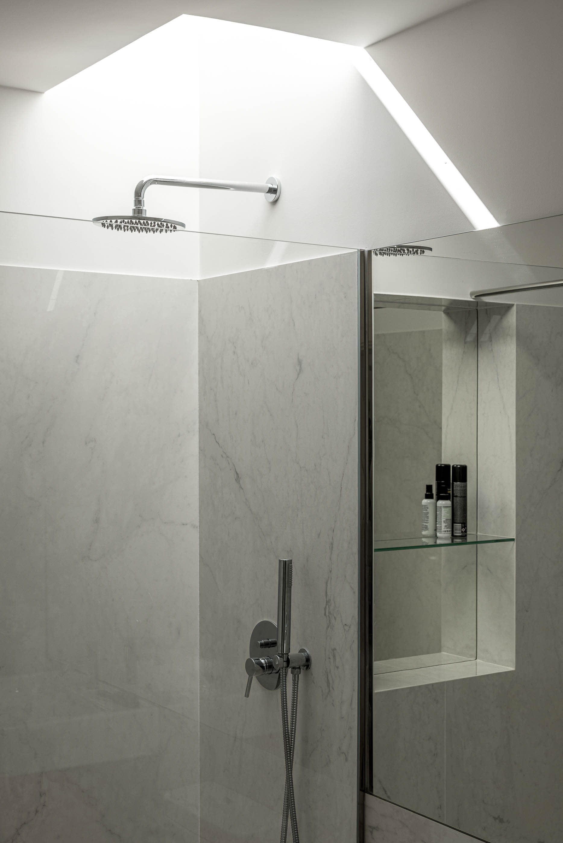 Casa de banho: Detalhe do chuveiro embutido e nicho com prateleiras de vidro, revestimento em mármore branco. — Casa IMLA arquitetura Luppa em Porto