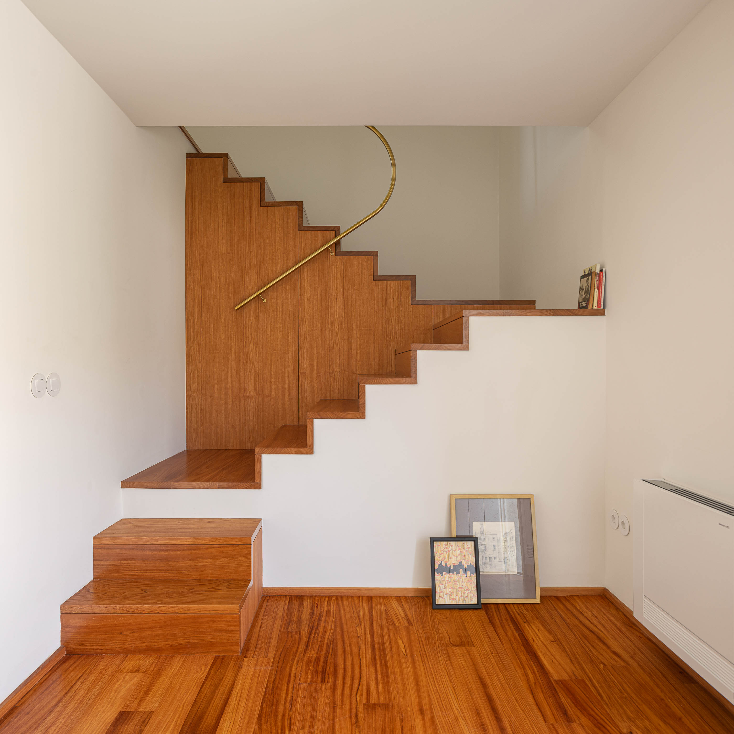 Escadas: Degraus em madeira clara, corrimão dourado curvo, pavimento em madeira e quadros decorativos. — Casa IMLA arquitetura Luppa em Porto