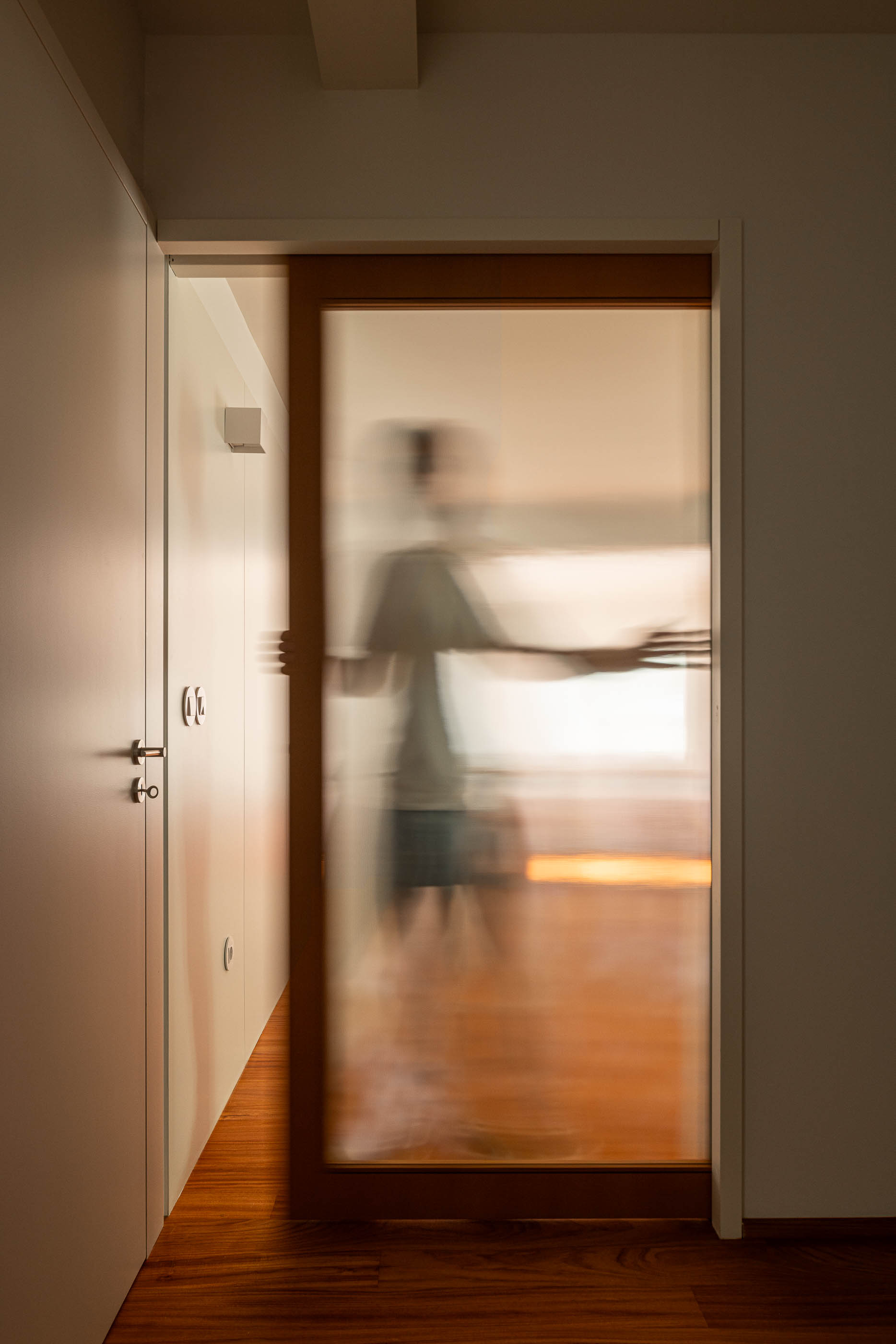 Closet: Porta de correr em vidro fosco com aro de madeira, corredor com roupeiros brancos. — Casa IMLA arquitetura Luppa em Porto