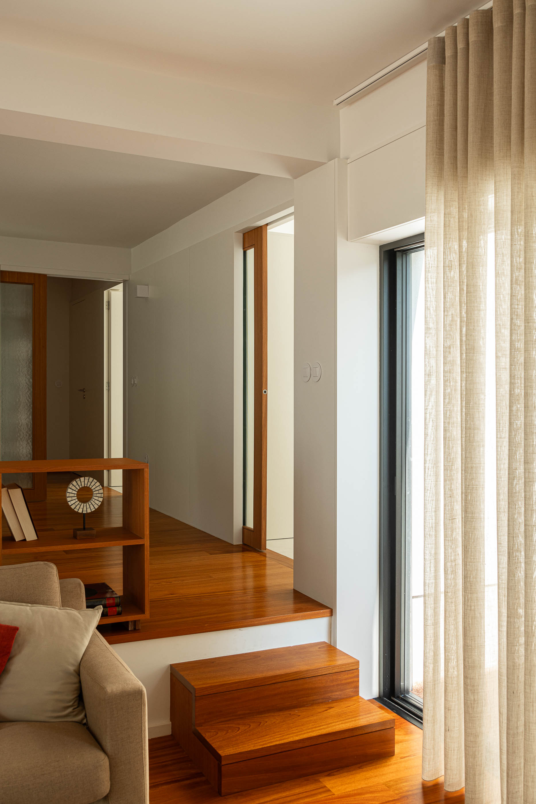 Sala de estar: Estante de madeira, sofá bege, cortinas claras e pavimento em madeira. — Casa IMLA arquitetura Luppa em Porto
