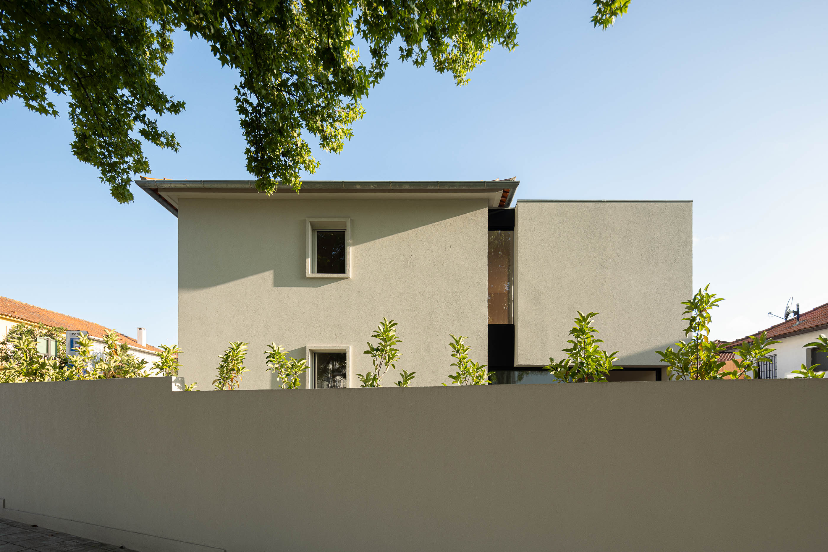 Exterior: Fachada da casa com muro branco, vegetação e céu azul. — Casa IMLA arquitetura Luppa em Porto