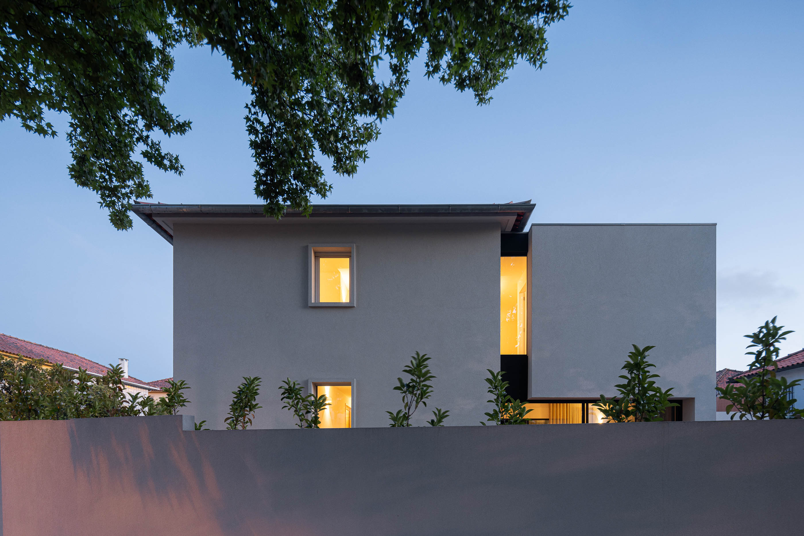 Exterior: Vista noturna da fachada da casa com muro branco e iluminação. — Casa IMLA arquitetura Luppa em Porto