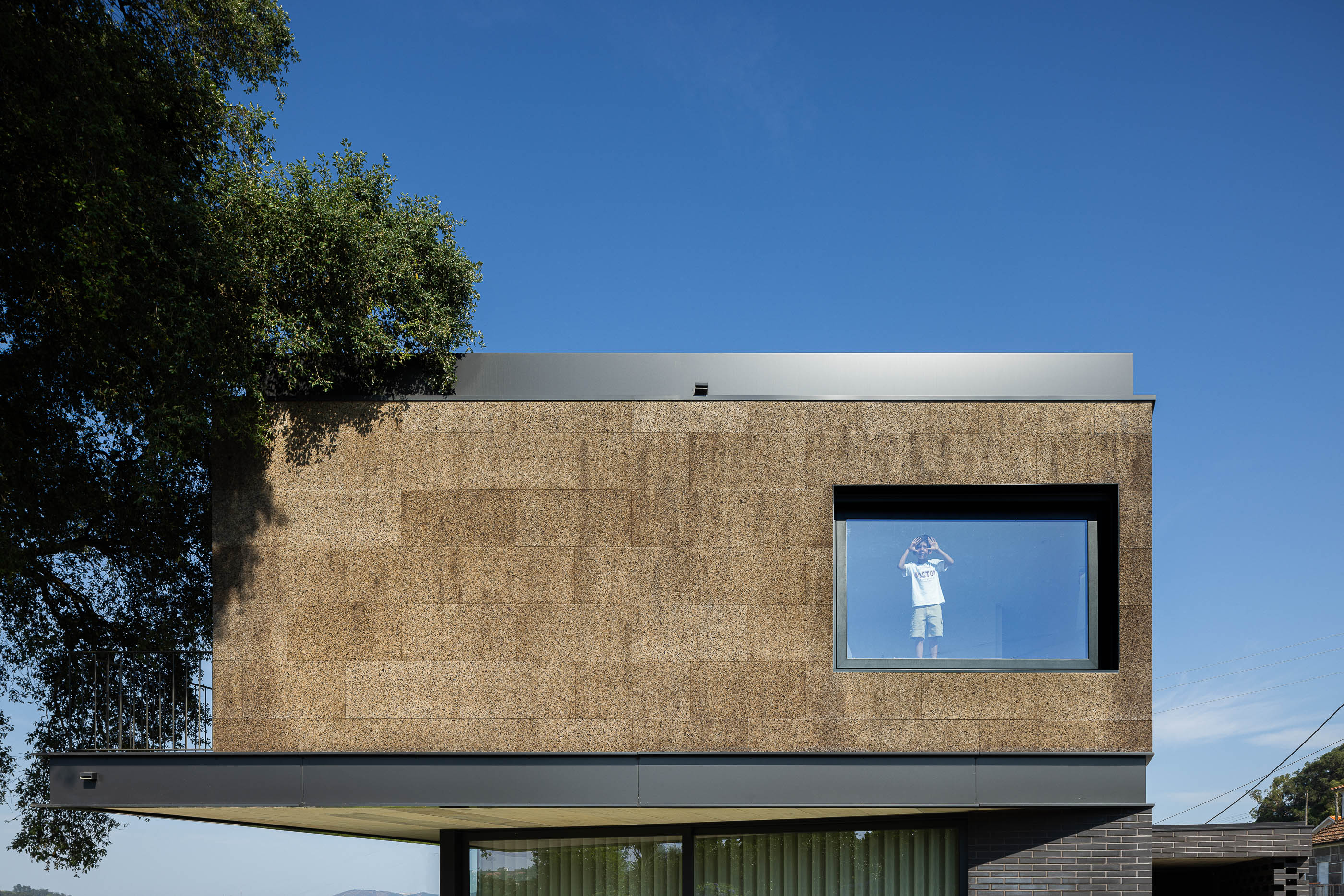 Fachada: Detalhe do revestimento de cortiça no piso superior e janela com moldura preta. — Casa do Sobreiro arquitetura Skemba - Arquitectura e Engenharia em Amarante