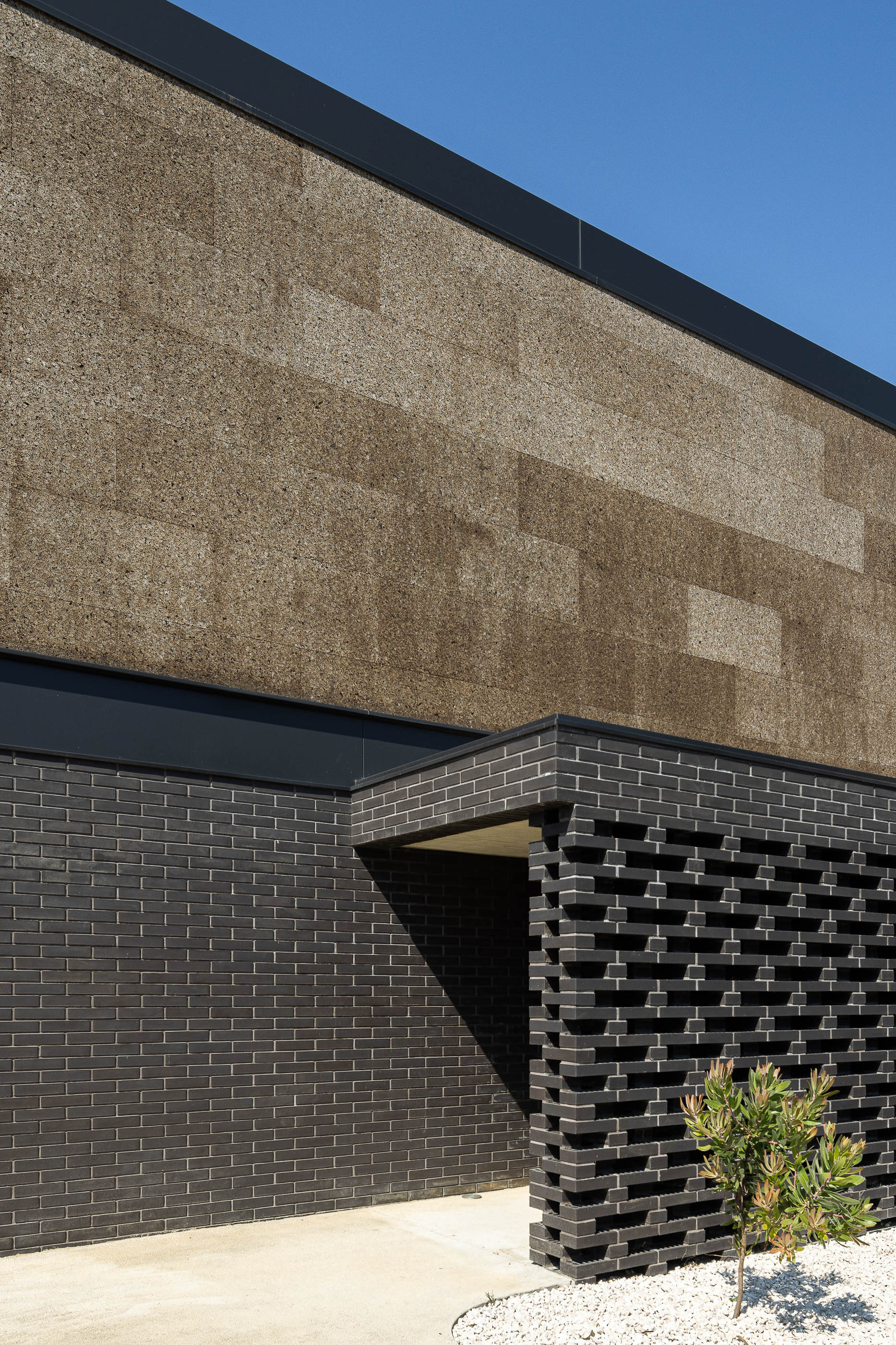 Entrada: Detalhe da fachada com revestimento de cortiça e tijolo preto, com elementos vazados. — Casa do Sobreiro arquitetura Skemba - Arquitectura e Engenharia em Amarante