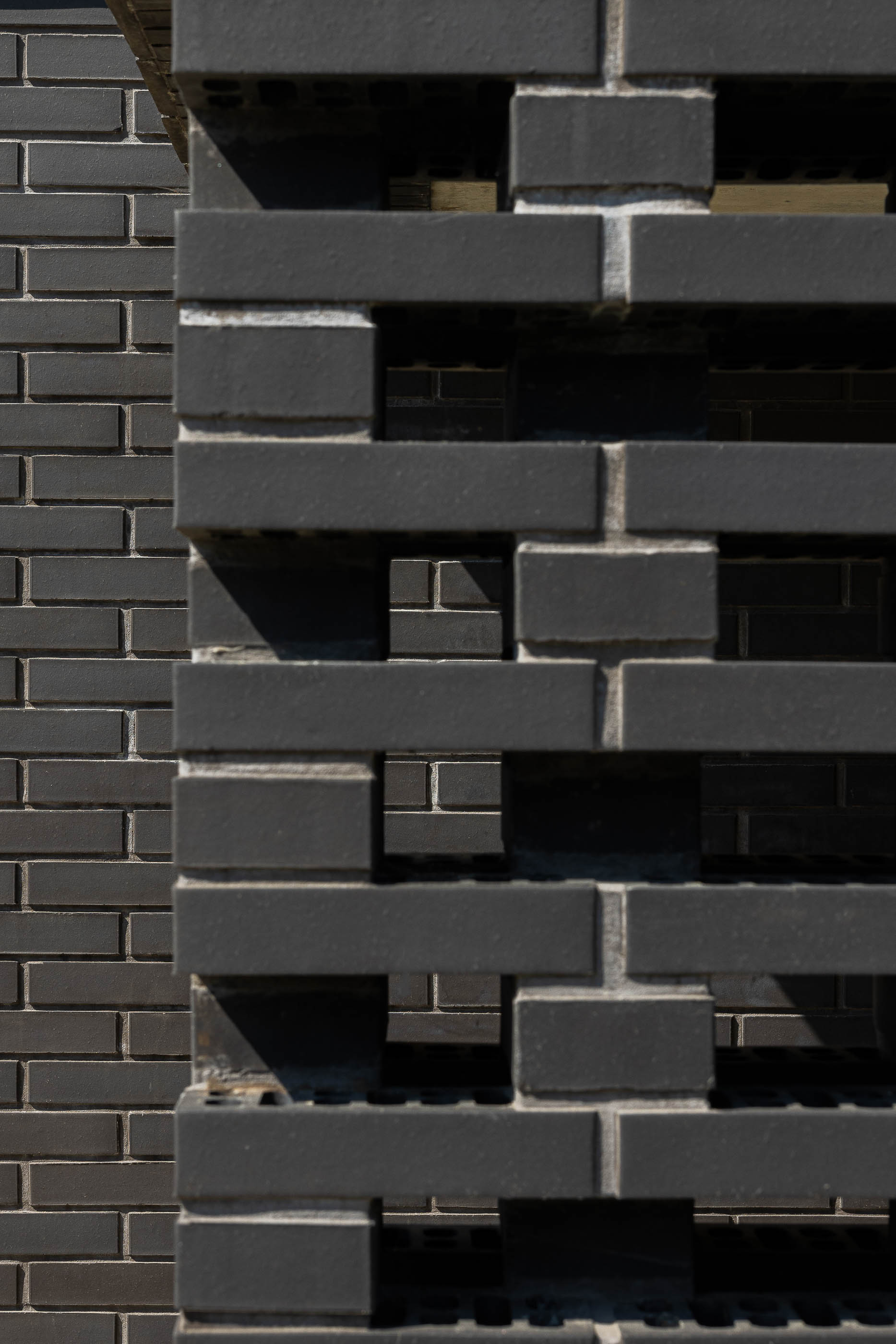 Entrada: Close-up da parede de tijolo preto com elementos vazados, criando um efeito de sombra e luz. — Casa do Sobreiro arquitetura Skemba - Arquitectura e Engenharia em Amarante