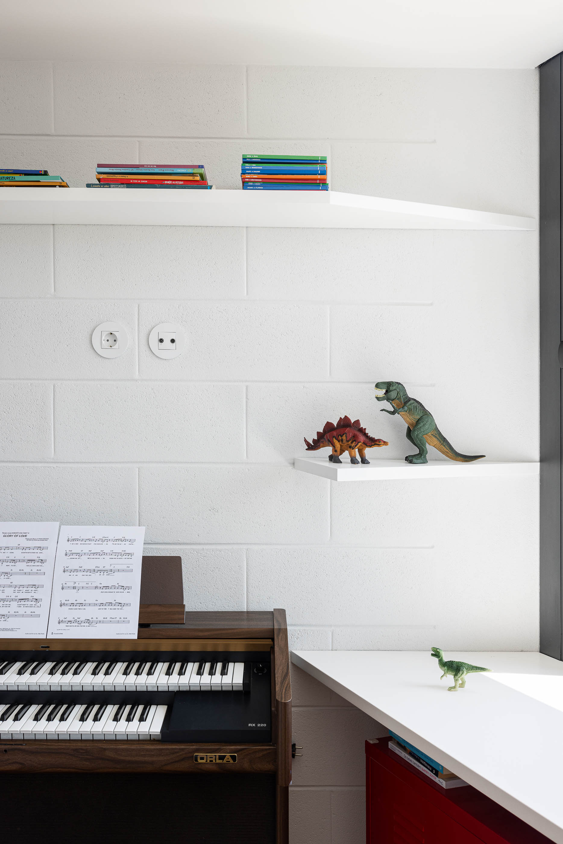 Quarto: Detalhe da parede branca texturizada com prateleiras, livros e brinquedos, com um órgão ao lado. — Casa do Sobreiro arquitetura Skemba - Arquitectura e Engenharia em Amarante