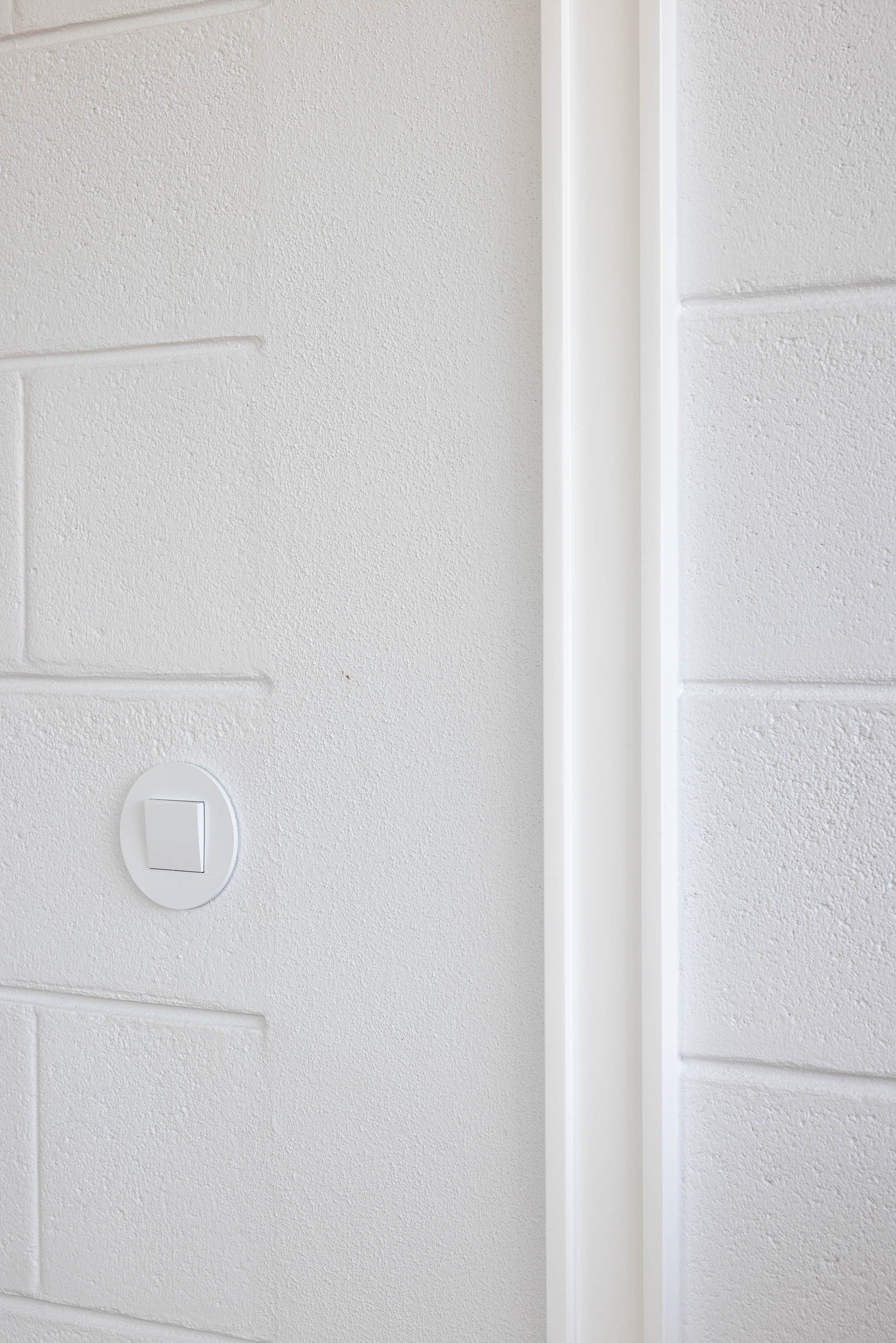 Quarto: Close-up da parede branca texturizada com interruptor e moldura da porta. — Casa do Sobreiro arquitetura Skemba - Arquitectura e Engenharia em Amarante