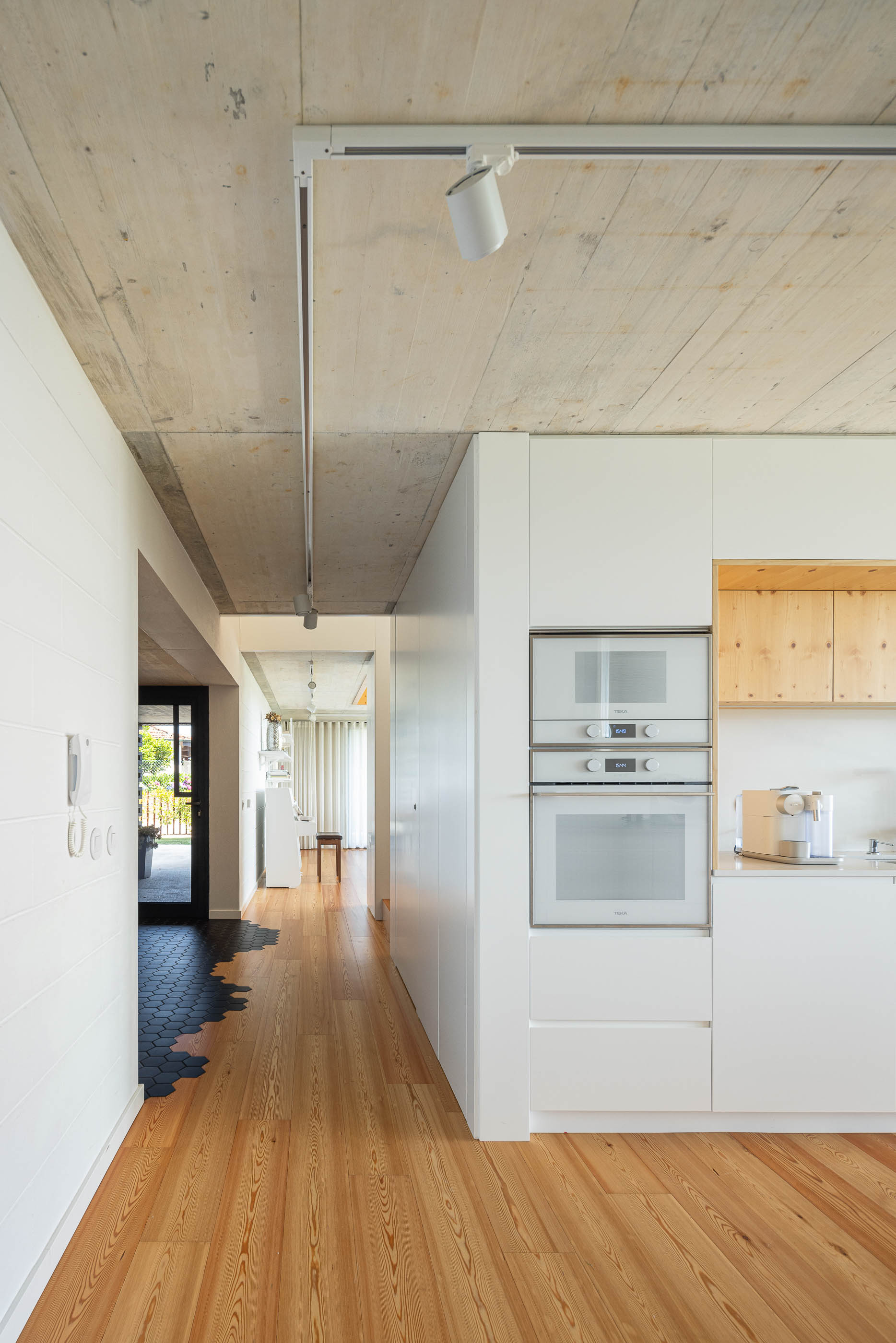 Cozinha: Vista da cozinha com armários brancos, bancada de madeira, pavimento de madeira e teto de betão aparente. — Casa do Sobreiro arquitetura Skemba - Arquitectura e Engenharia em Amarante