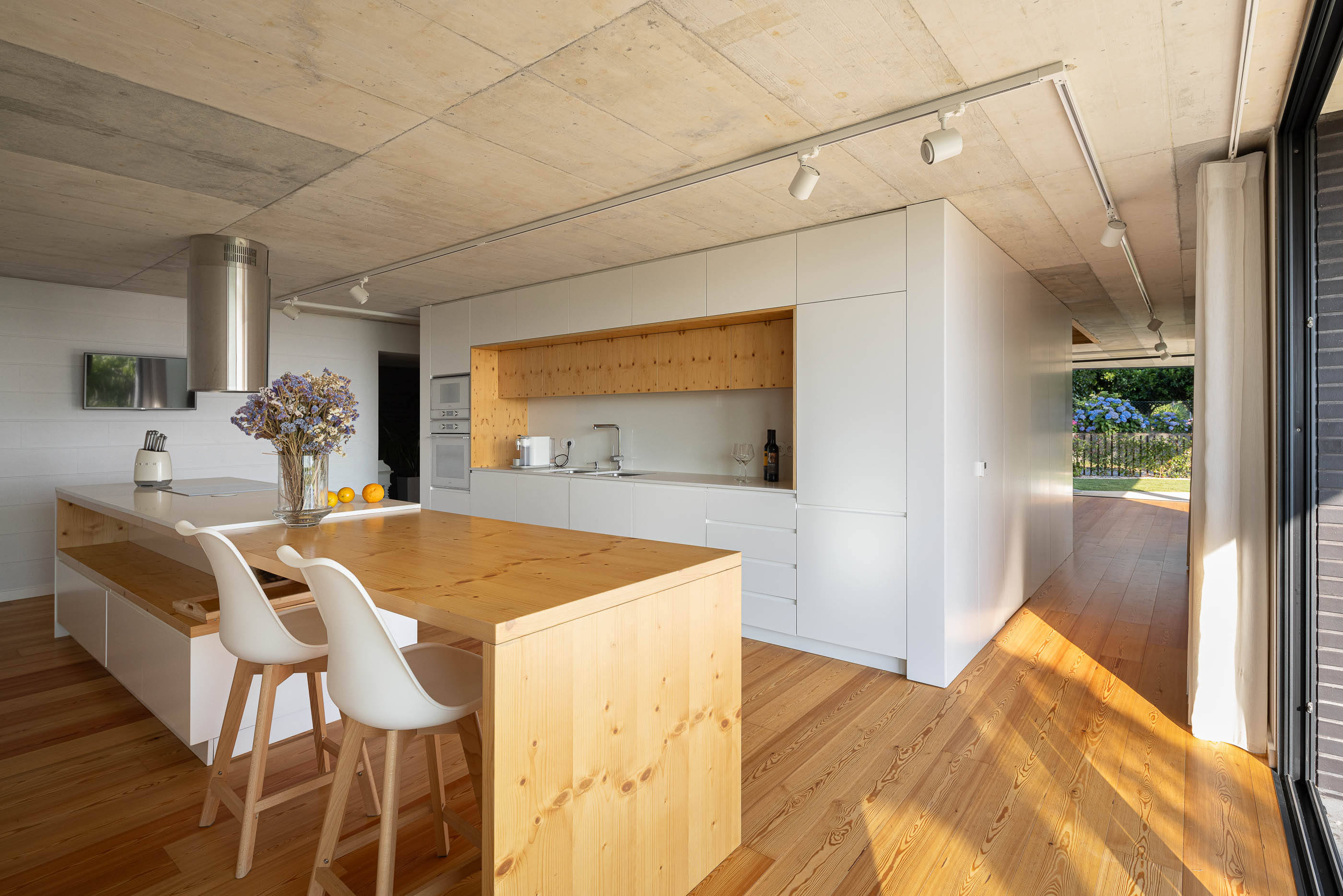 Cozinha: Detalhe da cozinha com armários brancos, teto de betão aparente e exaustor de inox. — Casa do Sobreiro arquitetura Skemba - Arquitectura e Engenharia em Amarante