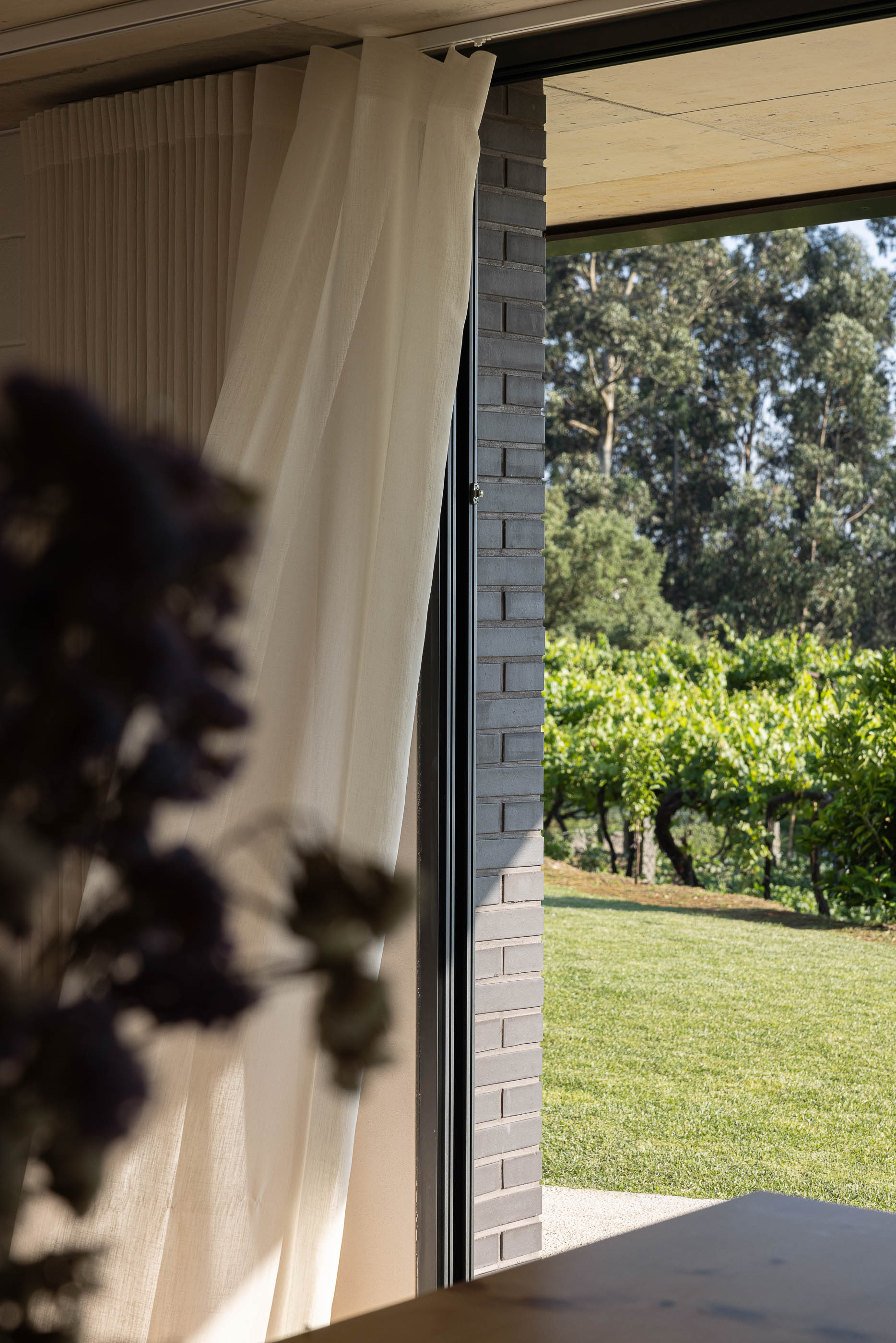 Exterior: Vista da fachada com revestimento de cortiça e tijolo preto, com varanda e bicicleta encostada. — Casa do Sobreiro arquitetura Skemba - Arquitectura e Engenharia em Amarante