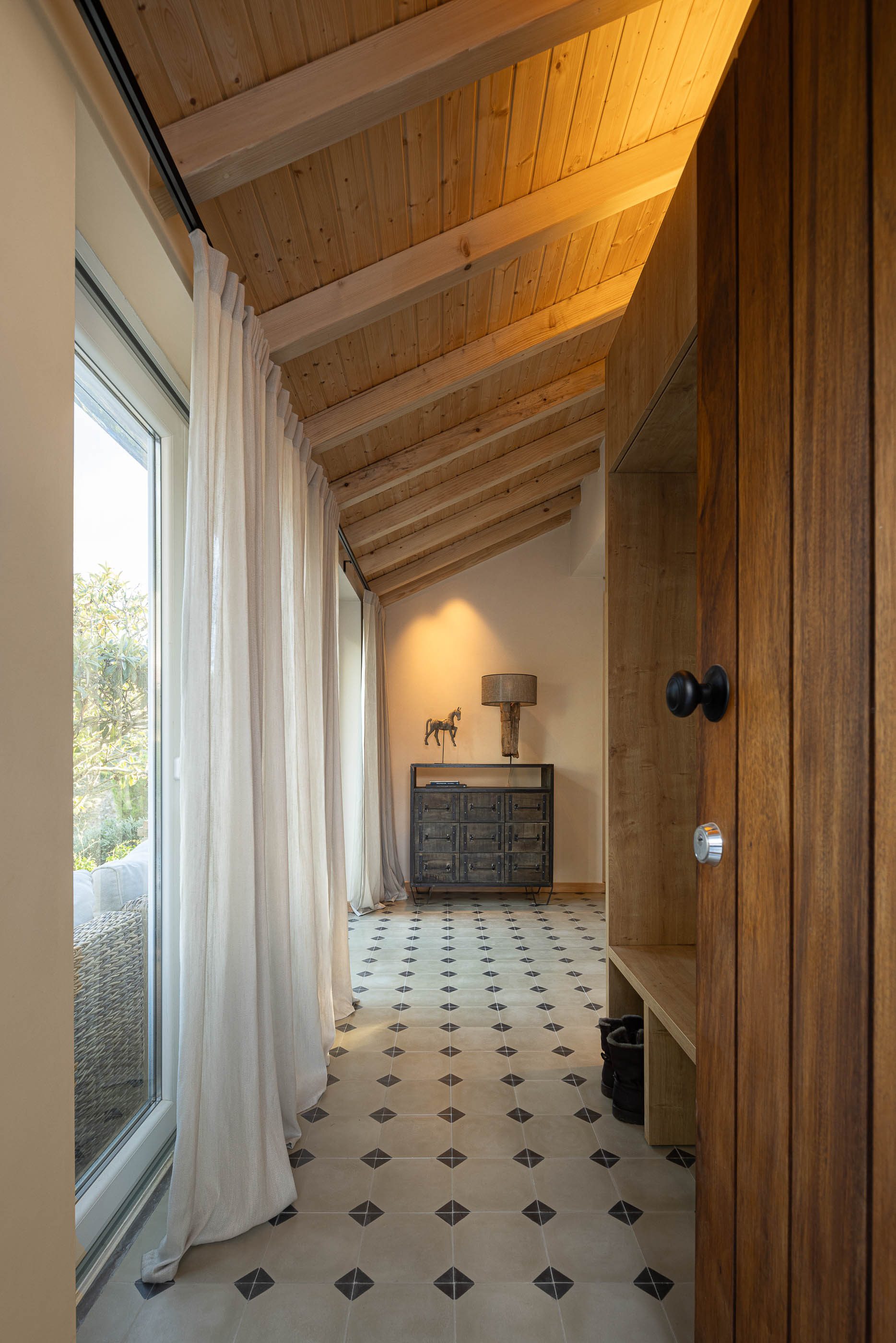 Entrada: Pavimento cerâmico com padrão, teto em madeira, armário em madeira clara e cortinas brancas. — Casa de Sintra arquitetura Tsou Arquitectos em Sintra
