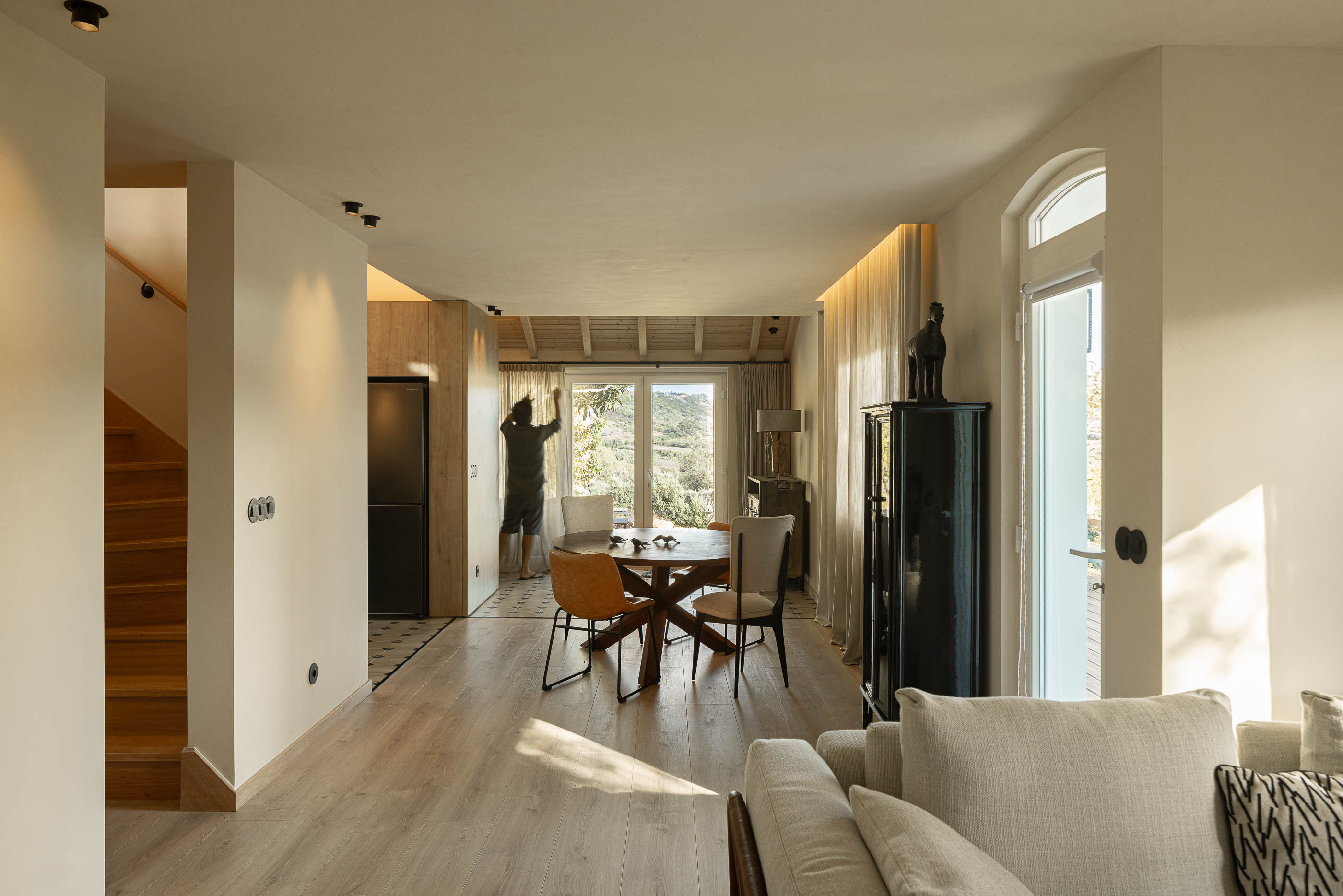Sala de estar/jantar: Espaço amplo com pavimento em madeira, mesa de jantar redonda e sofá em tons neutros. — Casa de Sintra arquitetura Tsou Arquitectos em Sintra